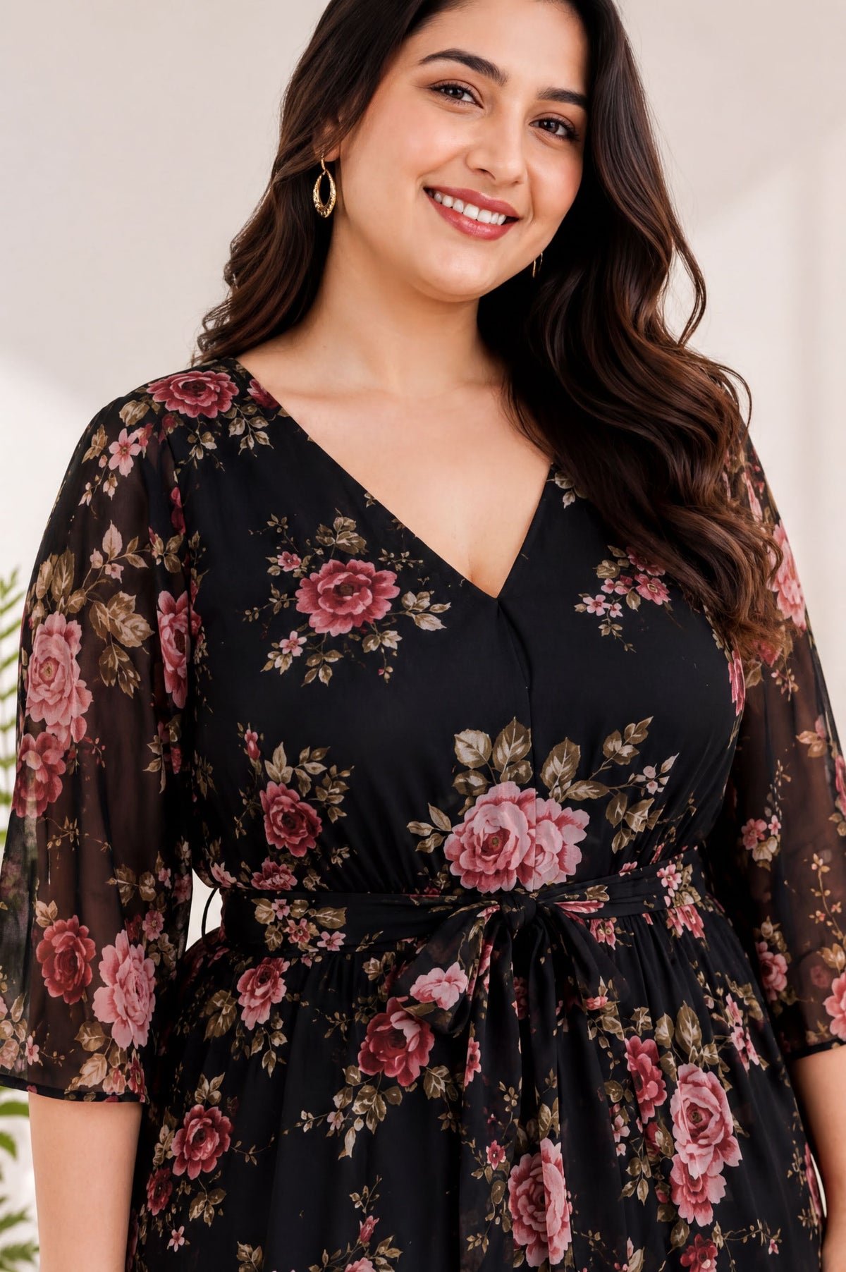 A woman with long, dark hair is smiling and wearing a black dress with a floral print.