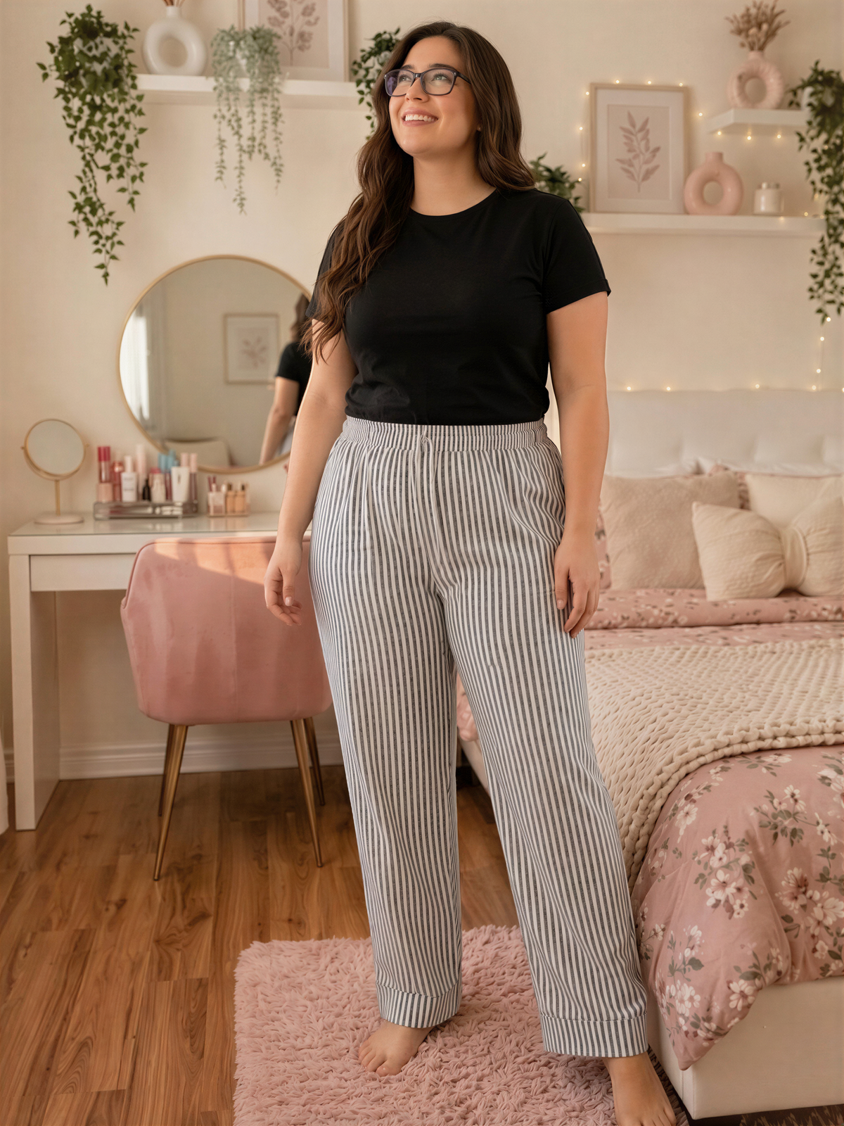 A woman wearing a black top and striped pants stands in a bedroom with a bed, dresser, and plants.