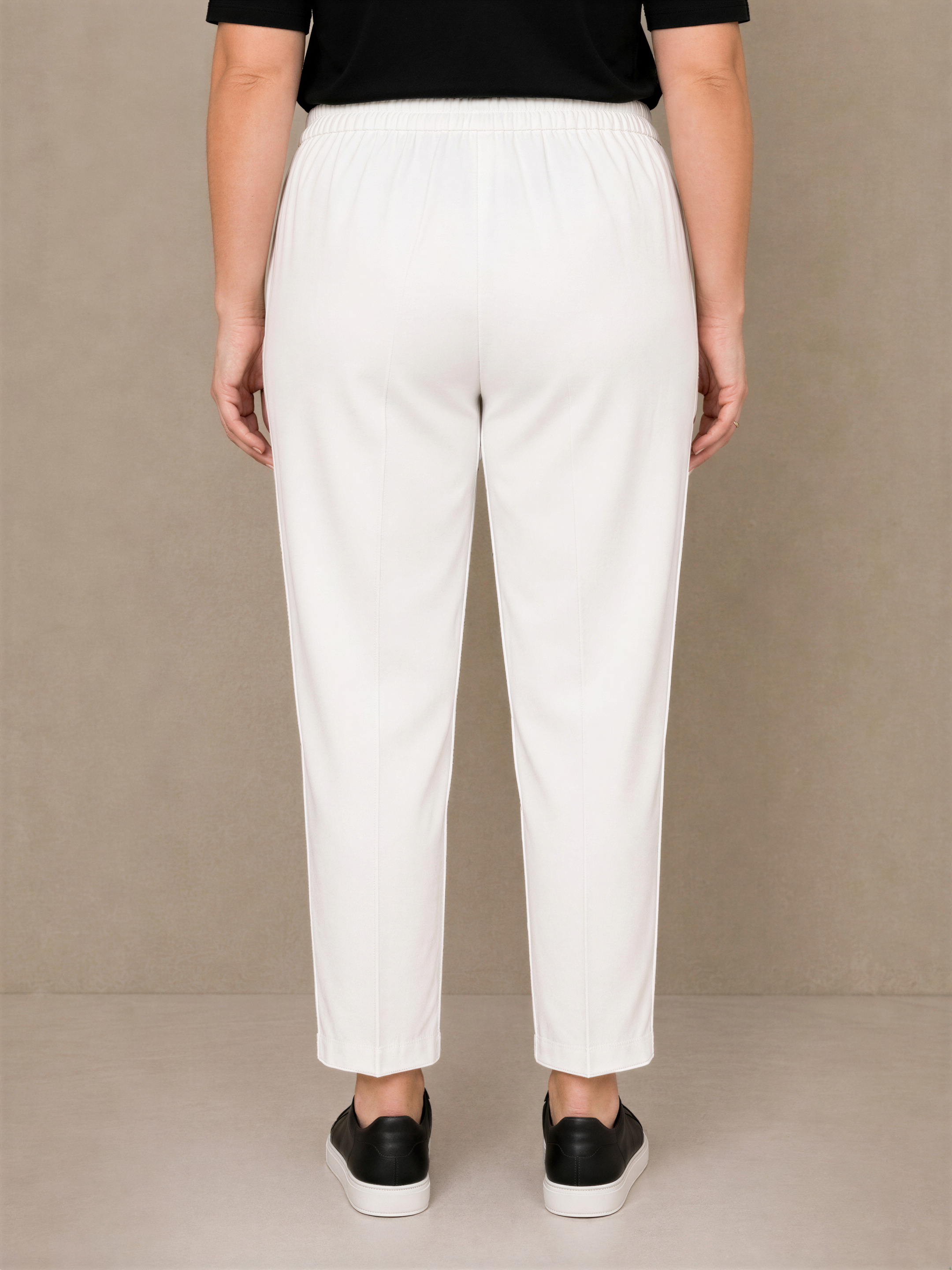 A person wearing white pants and black shoes is standing against a beige background.
