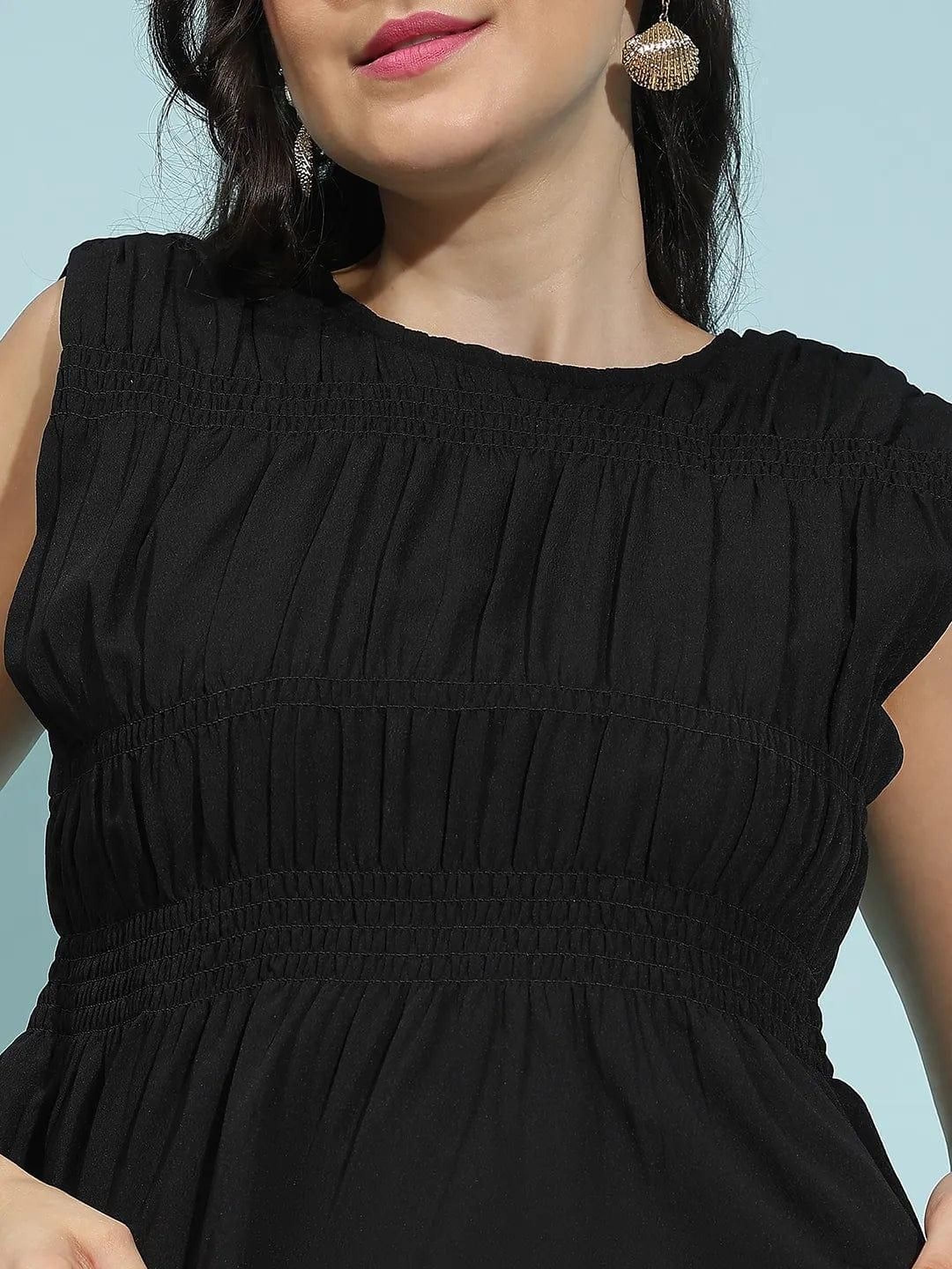A woman with dark hair wearing a black sleeveless top and a headband is smiling and looking to the side.
