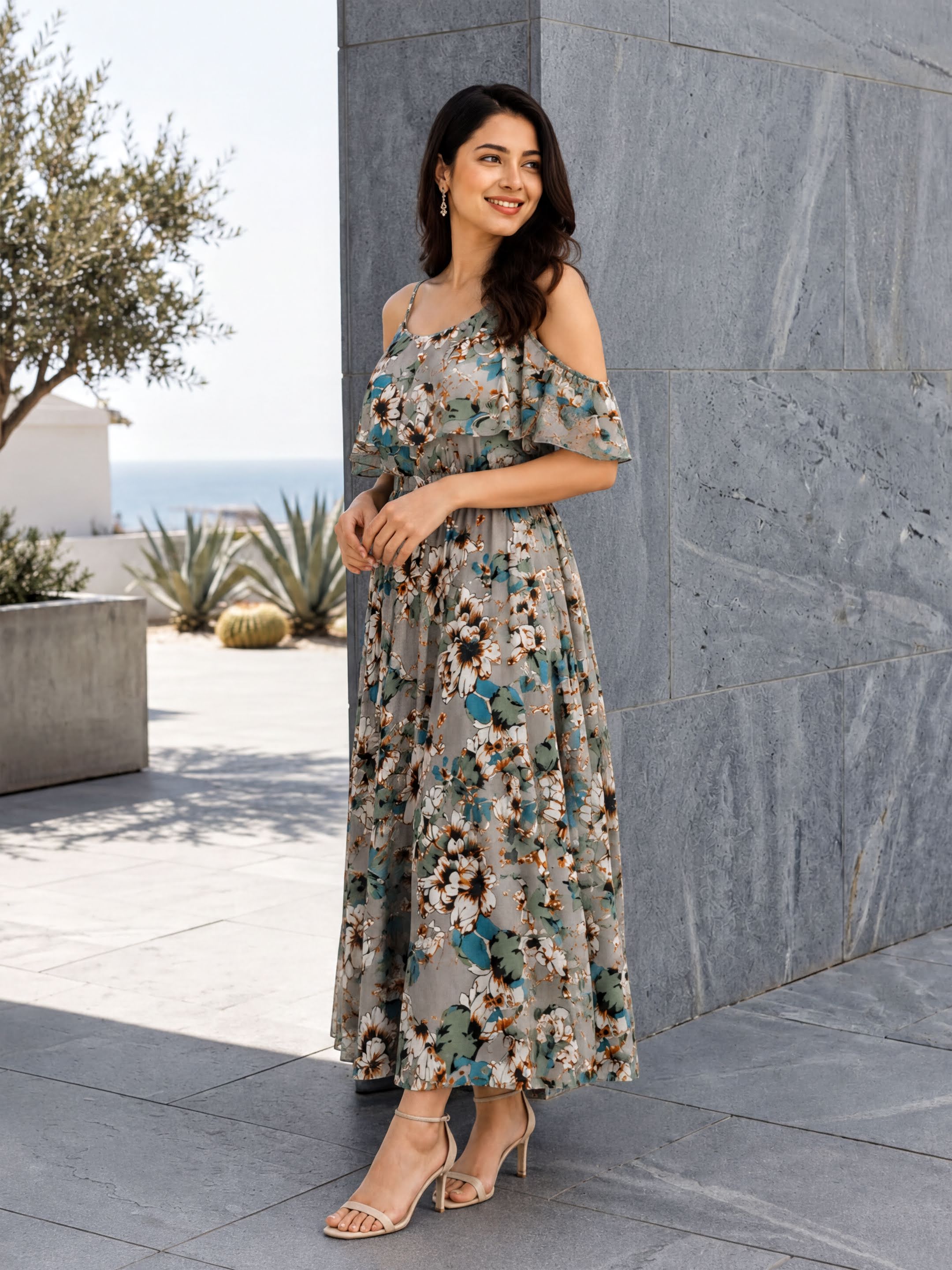 A woman wearing a floral print dress stands in front of a gray wall, smiling and posing for the camera.