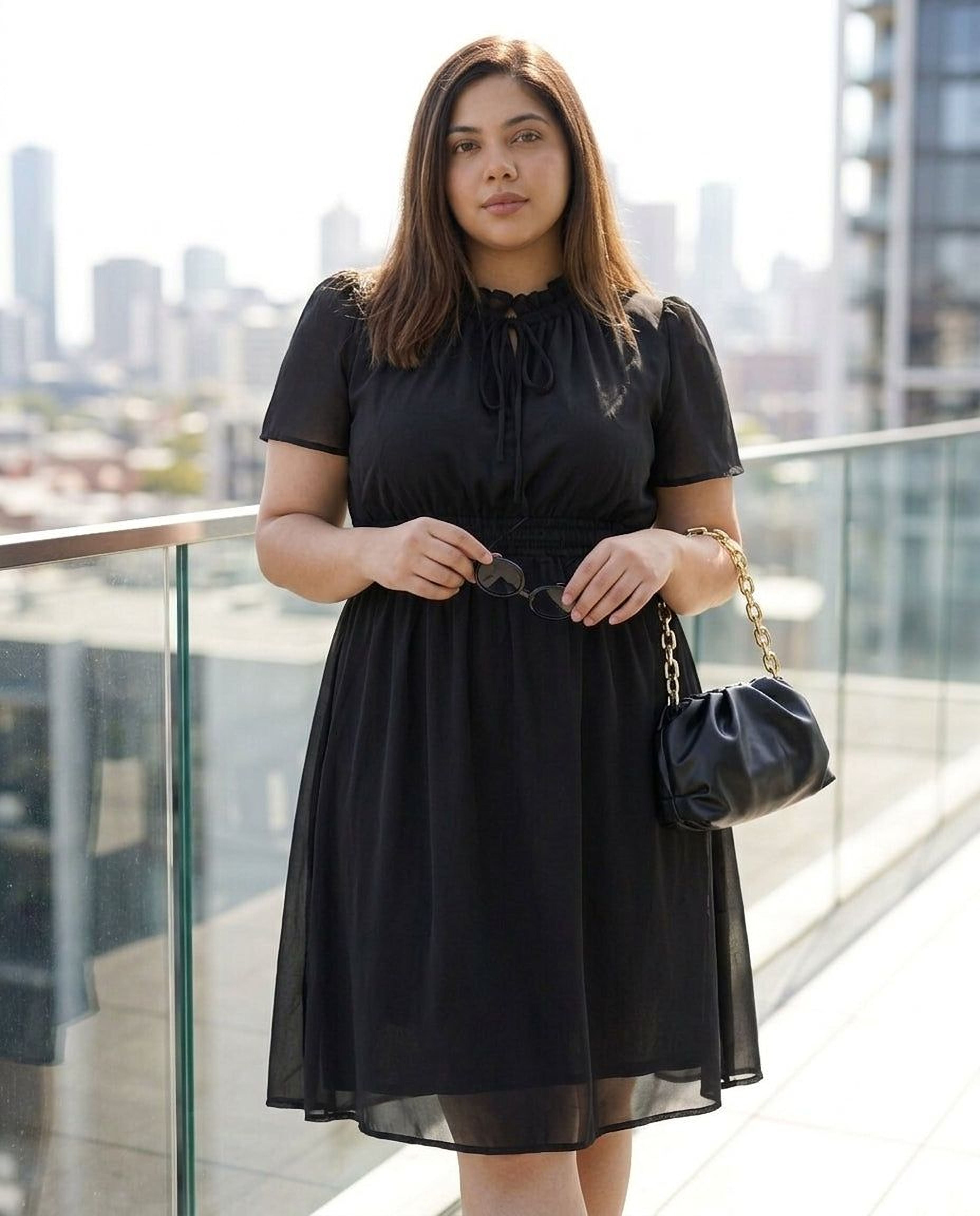 A woman wearing a black dress and high heels is smiling and looking down at her hand.