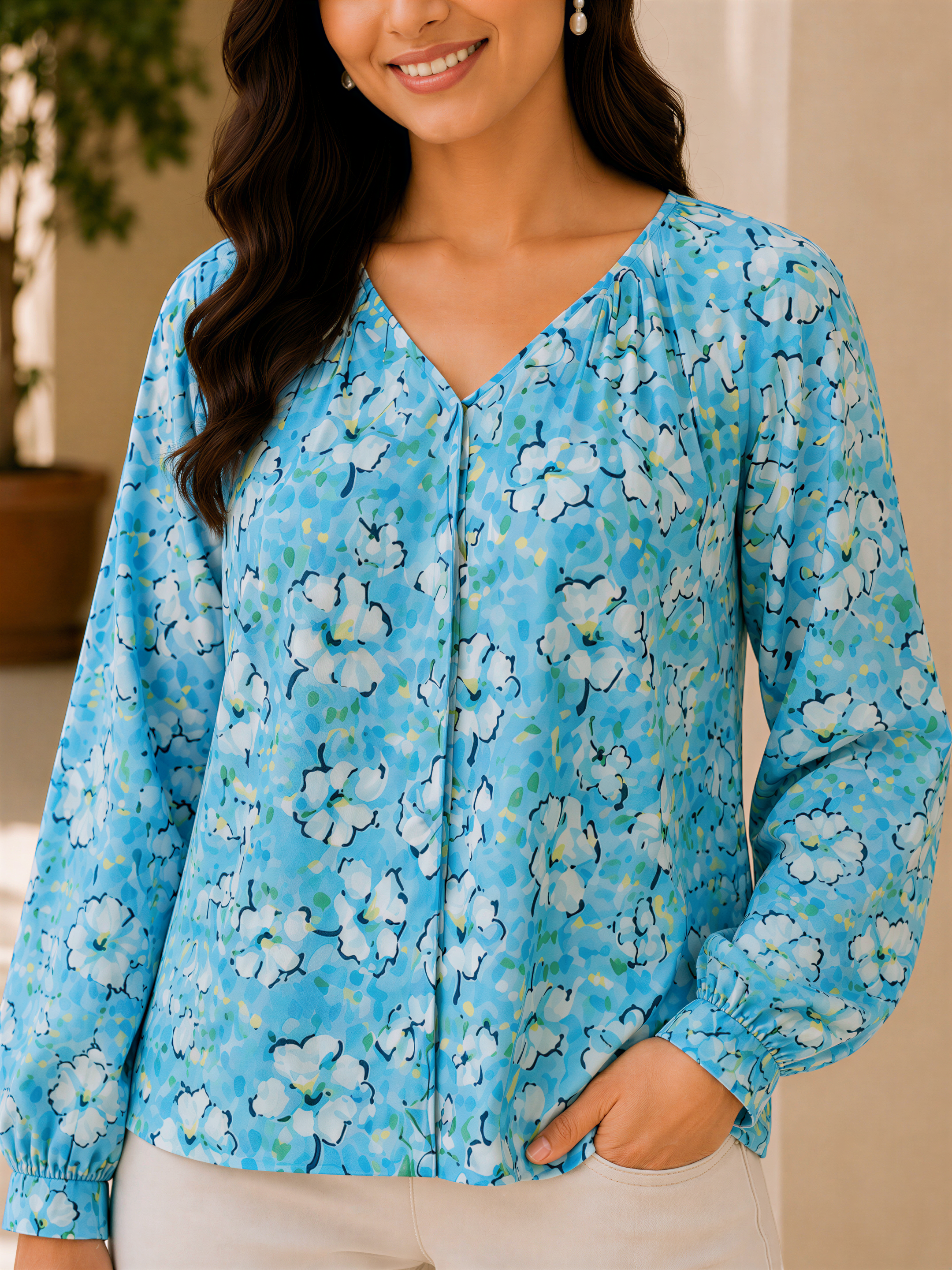 A woman wearing a blue floral blouse with long sleeves and a v neck, smiling at the camera.