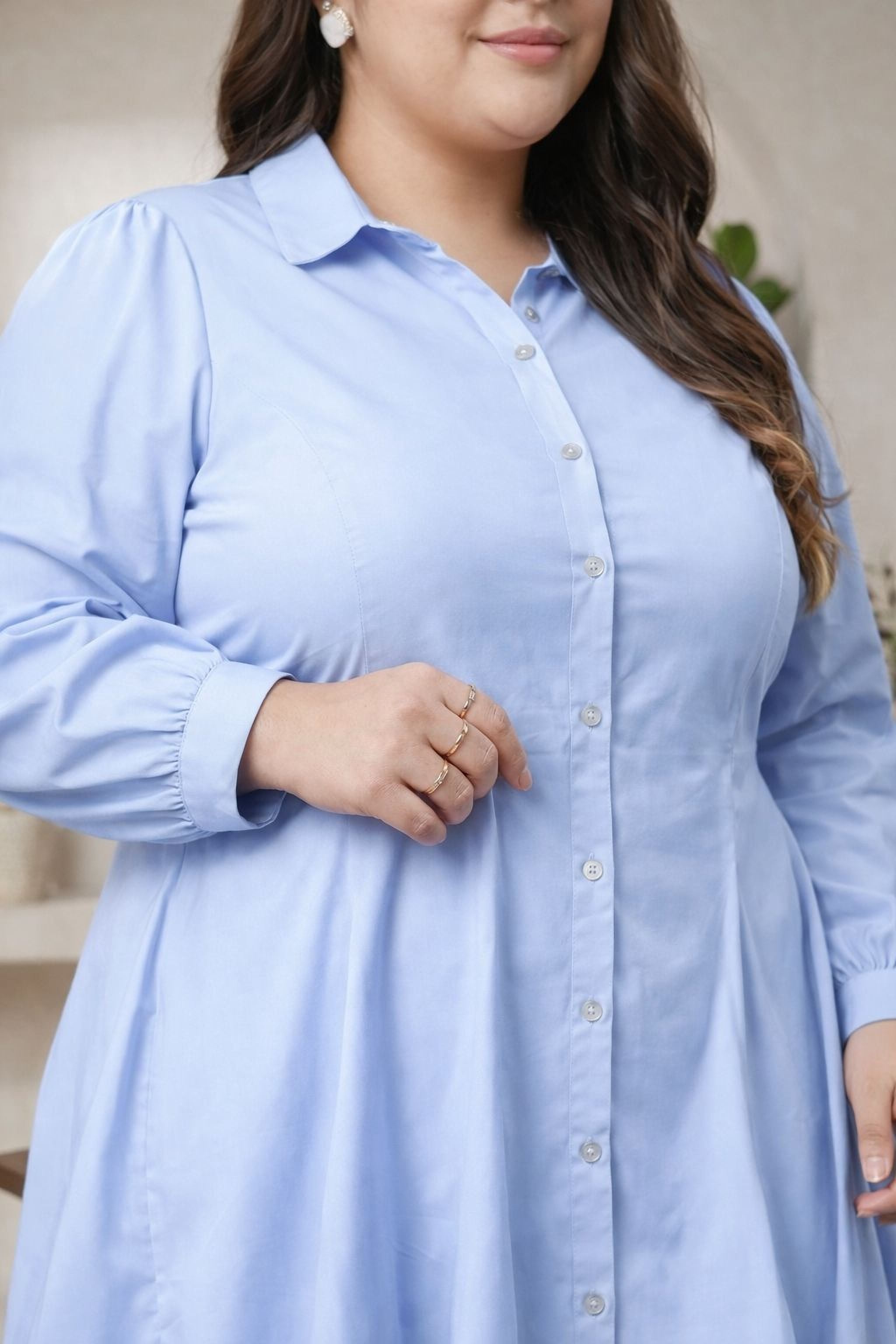 A woman wearing a light blue dress and sunglasses stands confidently against a white background.