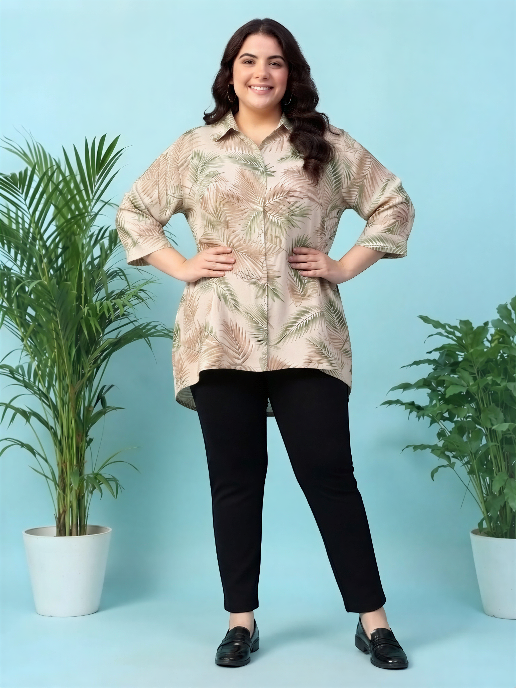 A woman wearing a floral print shirt and black pants stands in front of two potted plants against a blue background.