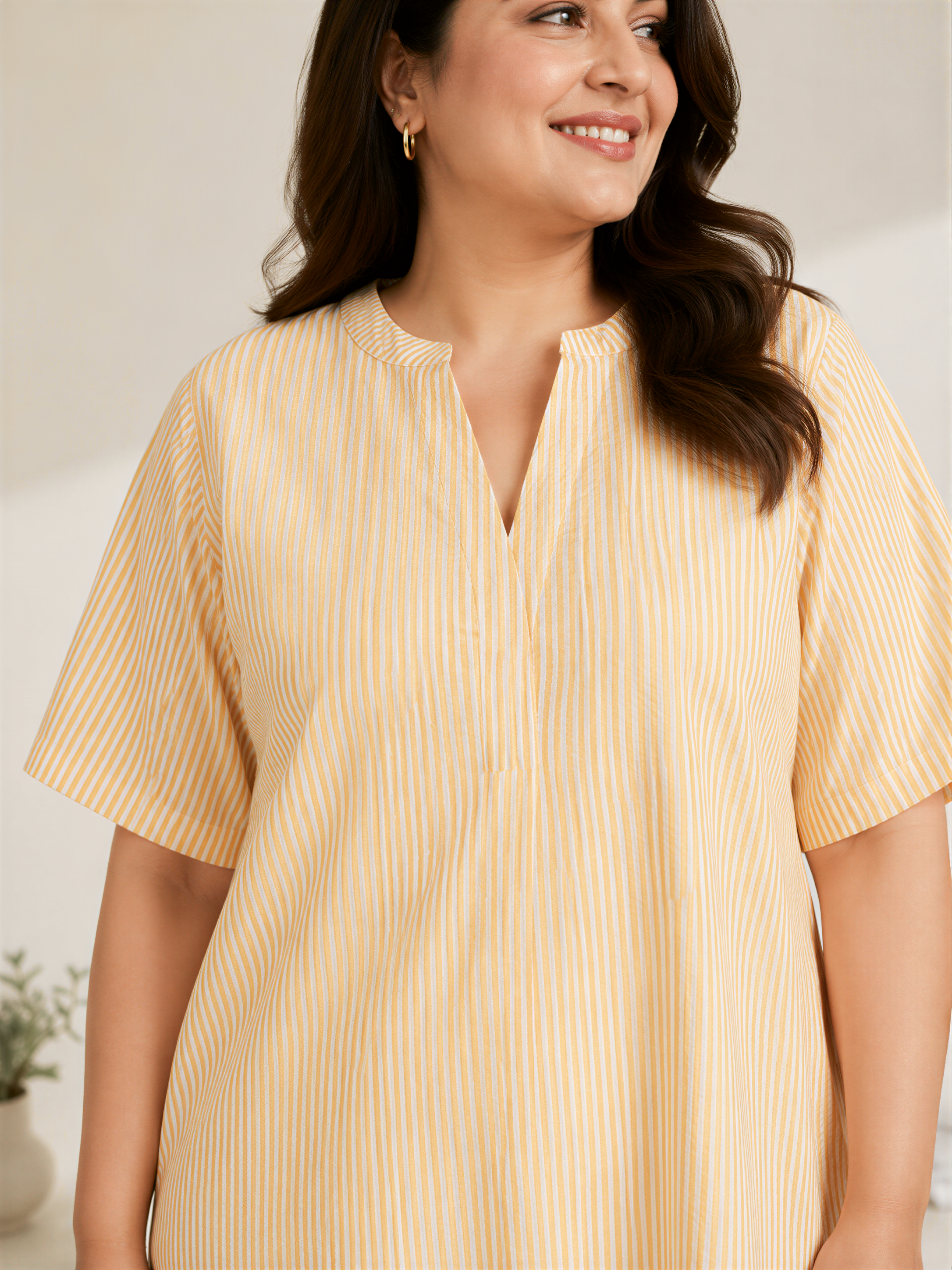 A woman with long dark hair is smiling and wearing a yellow and white striped dress.