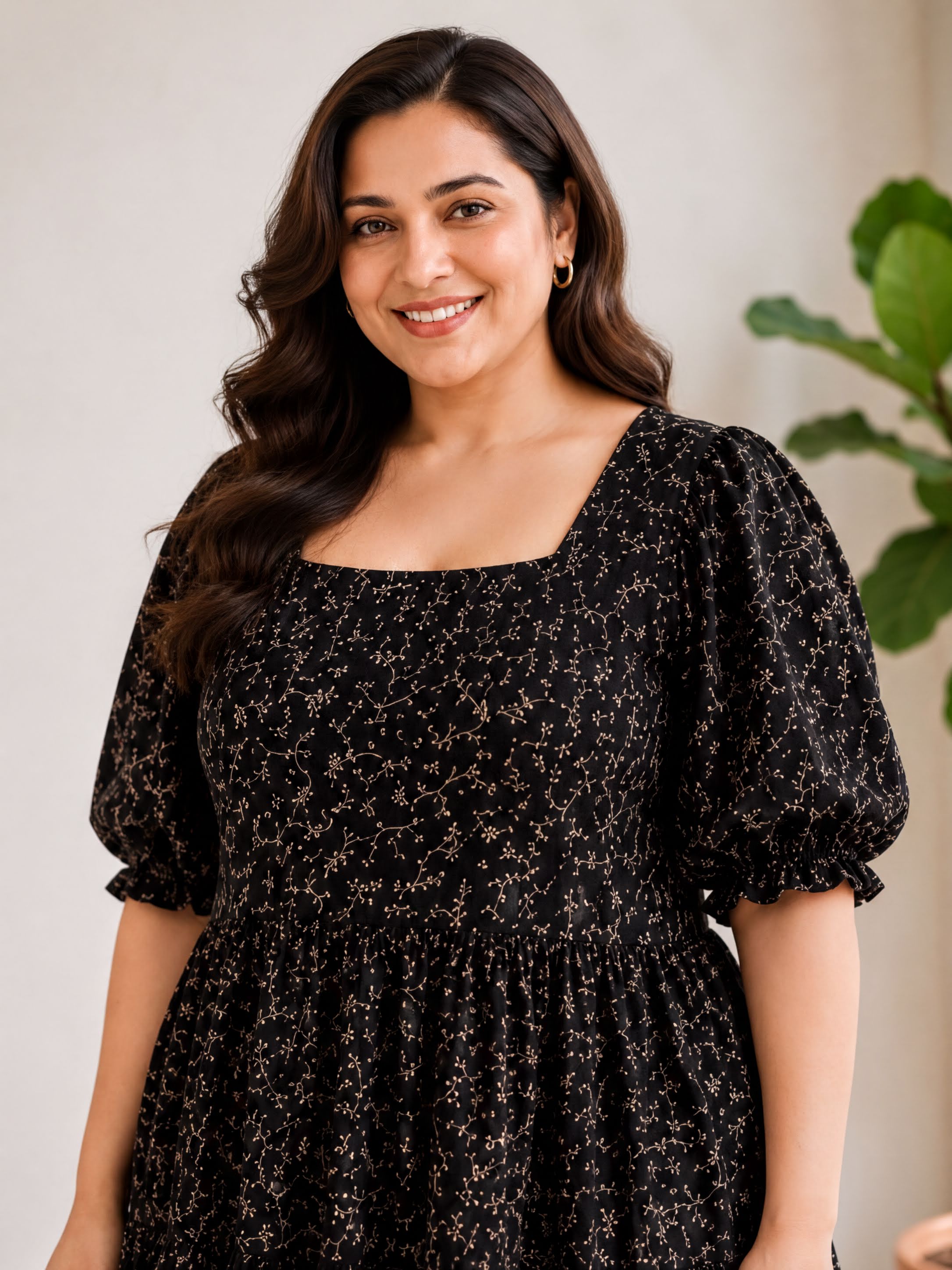 A woman with long brown hair is smiling and wearing a black dress with a floral pattern.
