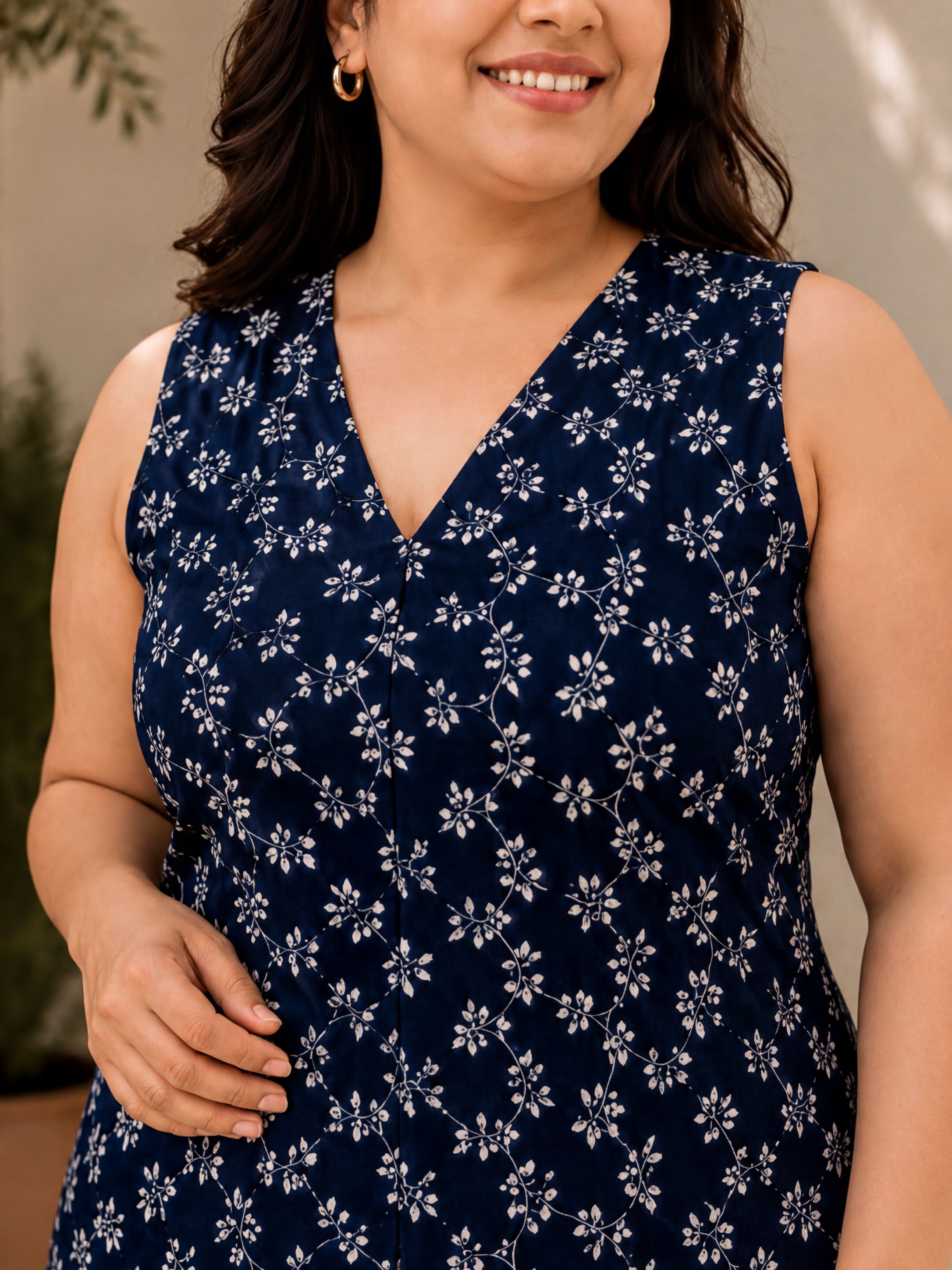 A woman wearing a sleeveless dress with a blue floral pattern, smiling at the camera.