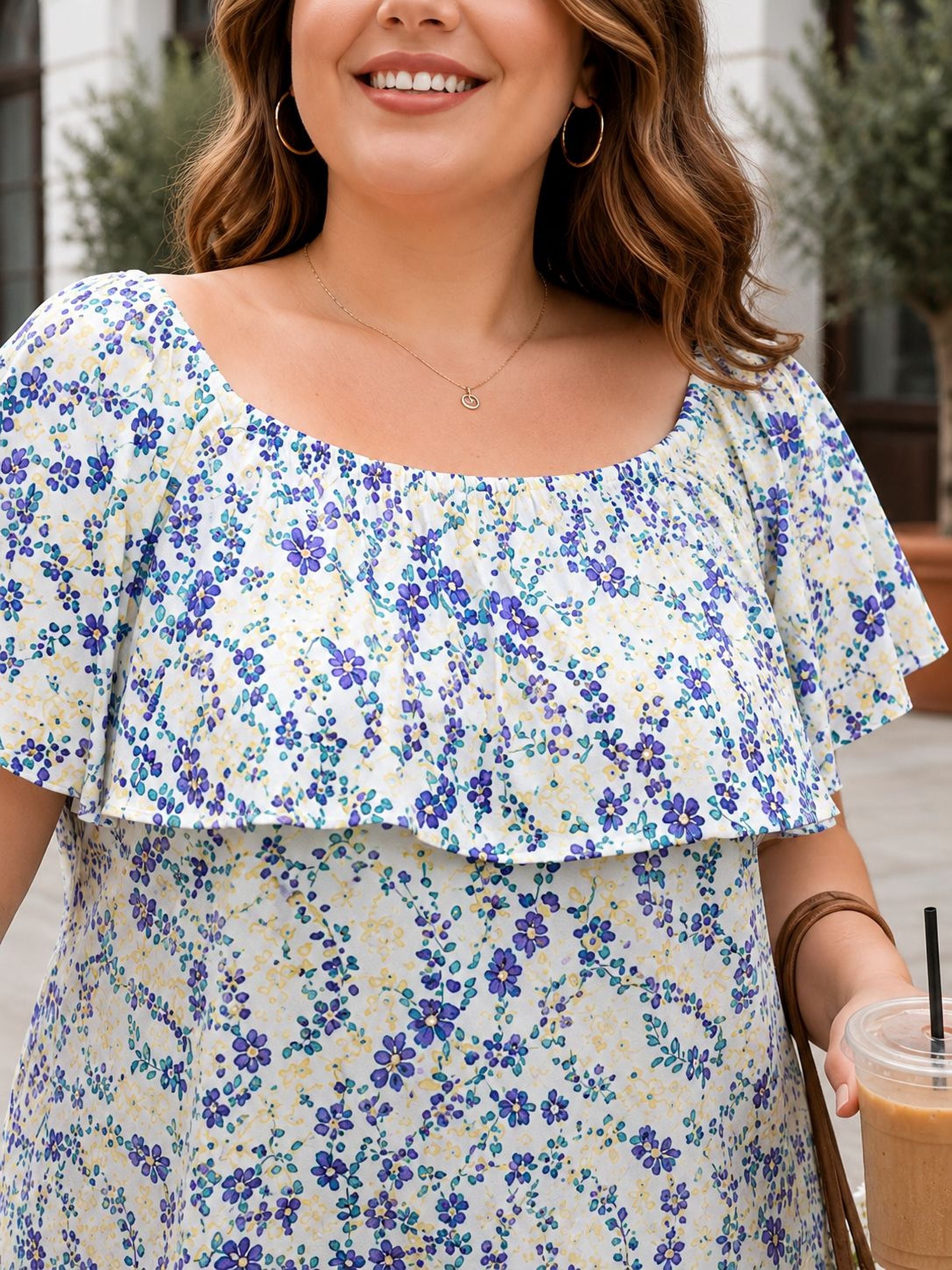 A woman wearing a white and blue floral dress is smiling and holding a drink in her hand.