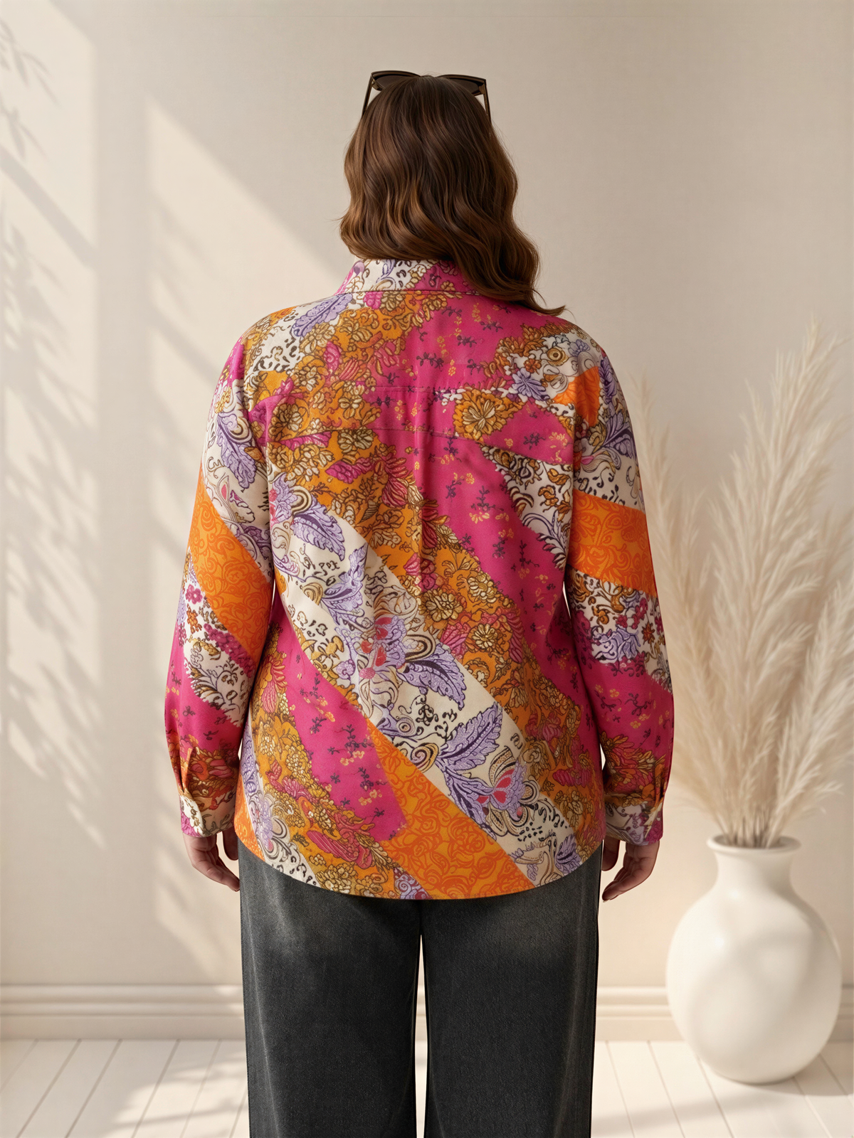 the back view of a person wearing a colorful, patterned shirt with long sleeves, standing in front of a white wall with a potted plant to the right.