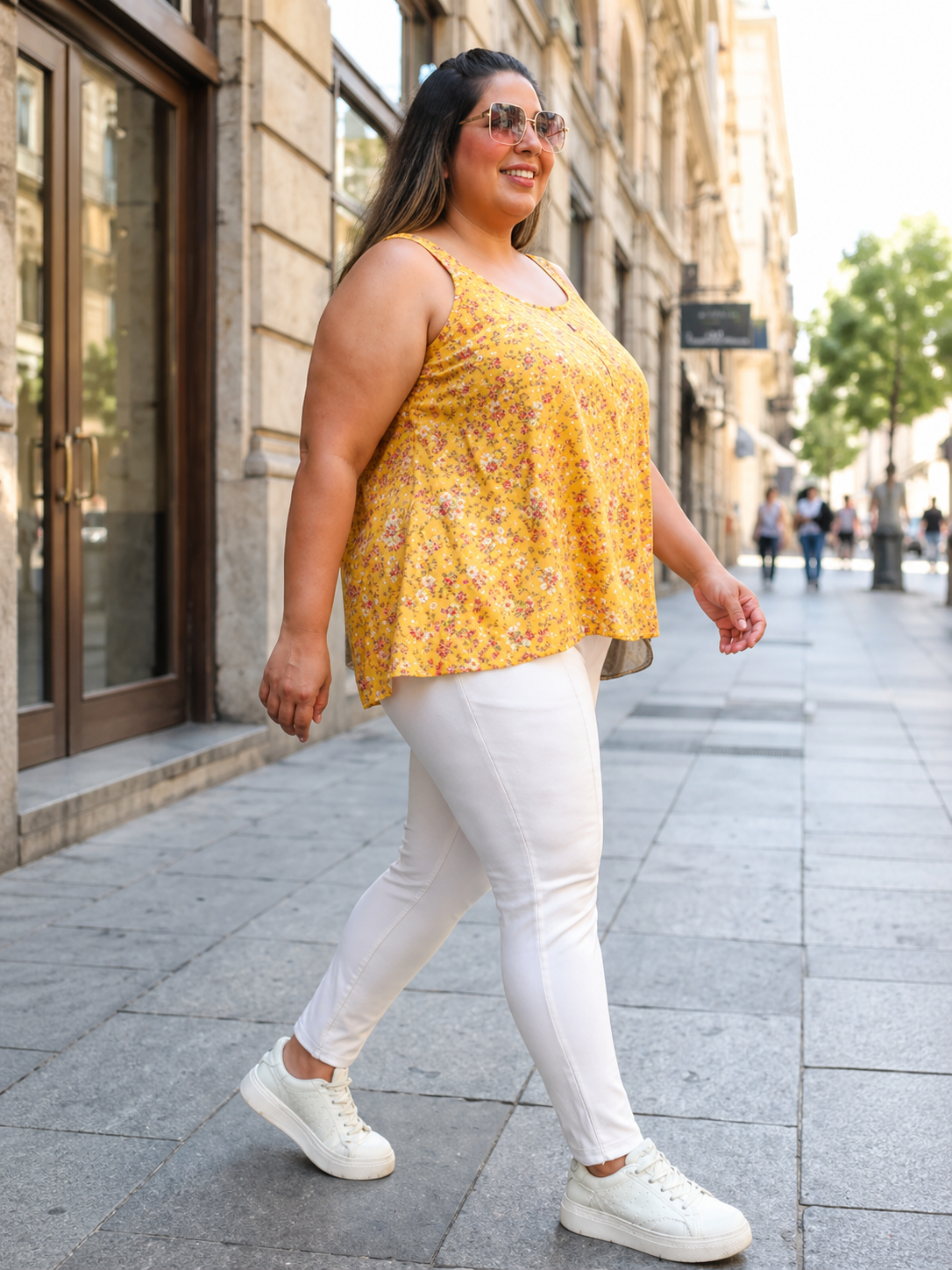 Plus size woman in yellow floral top and white jeans, walking outdoors on city street