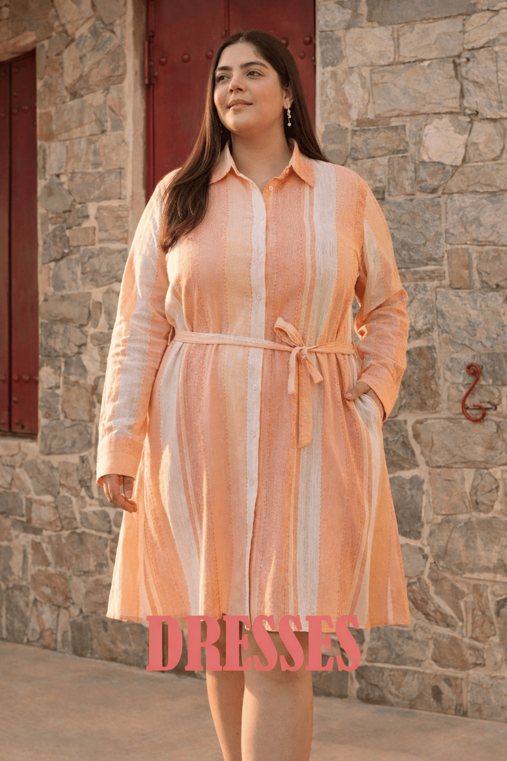 Woman wearing a peach striped dress standing in front of a stone wall.