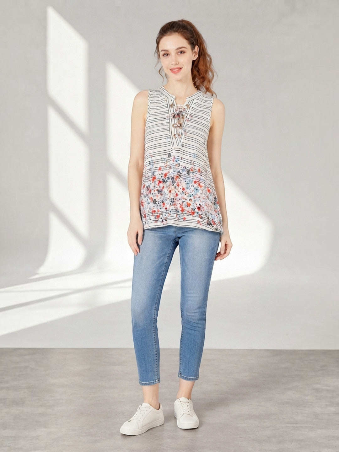 Striped floral sleeveless top with lace-up neckline, paired with blue jeans and white sneakers for casual women's fashion.