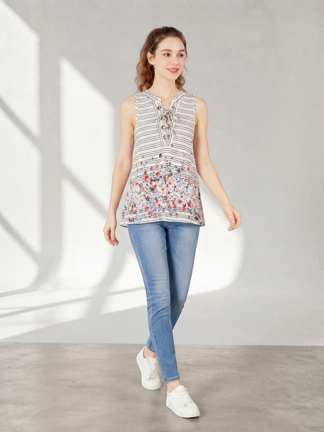 Woman wearing striped floral sleeveless top with lace-up neckline, paired with blue jeans and white sneakers