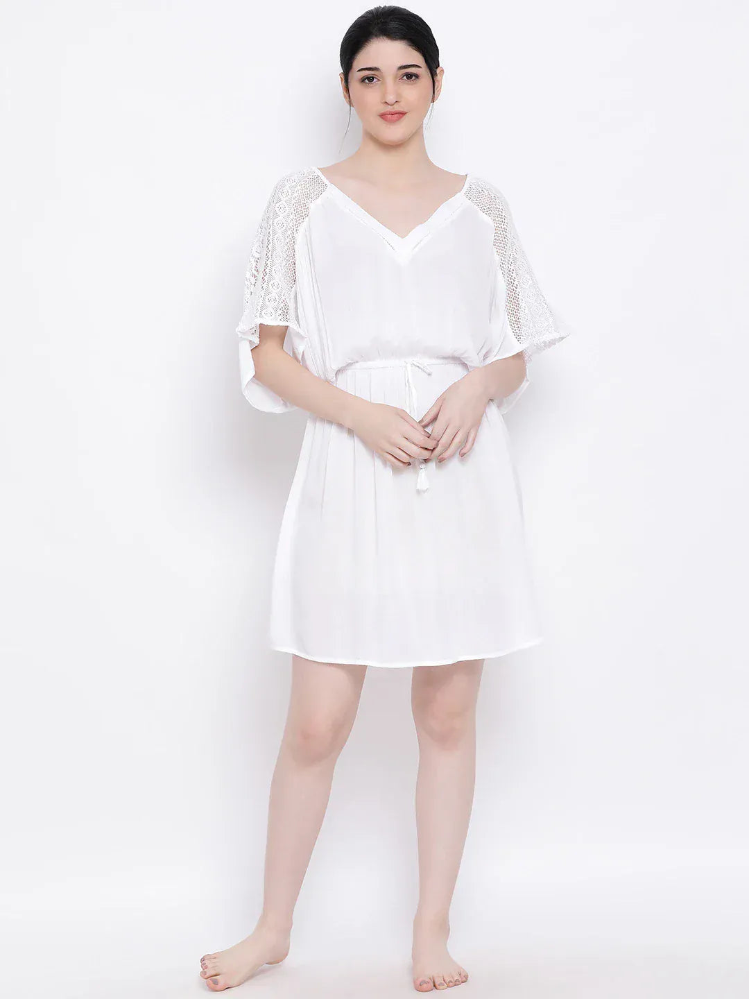 A woman wearing a white dress with lace sleeves and a v-neck, posing against a white background.