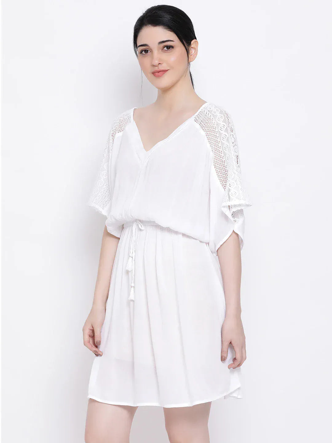 A woman wearing a white dress with lace sleeves and a v-neck, posing against a white background.