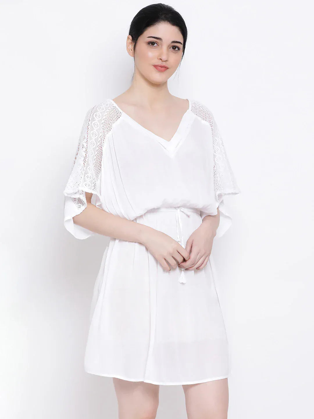 A woman wearing a white dress with lace sleeves and a v-neck, posing against a white background.