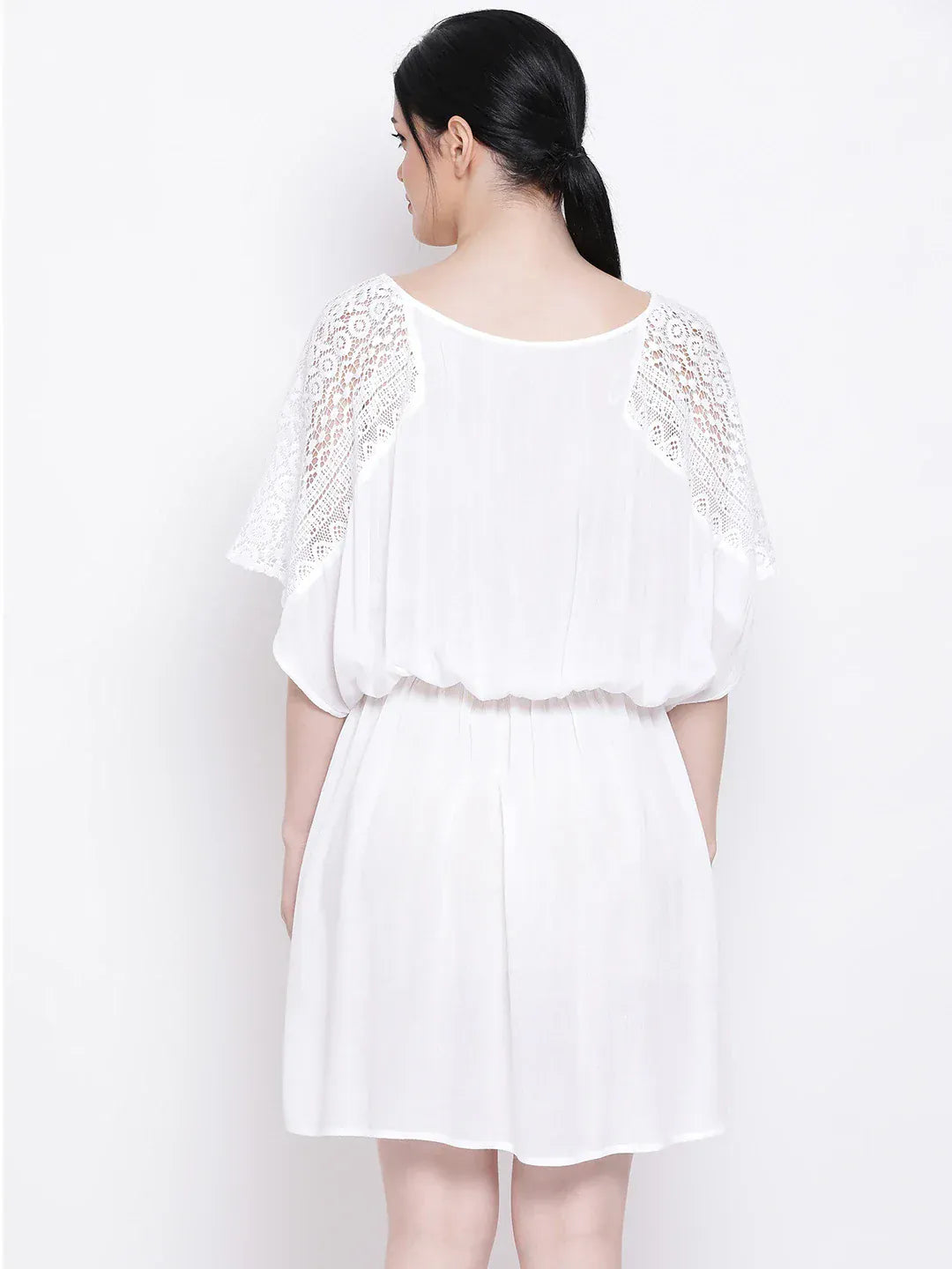 A woman wearing a white dress with lace sleeves and a v-neck, posing against a white background.
