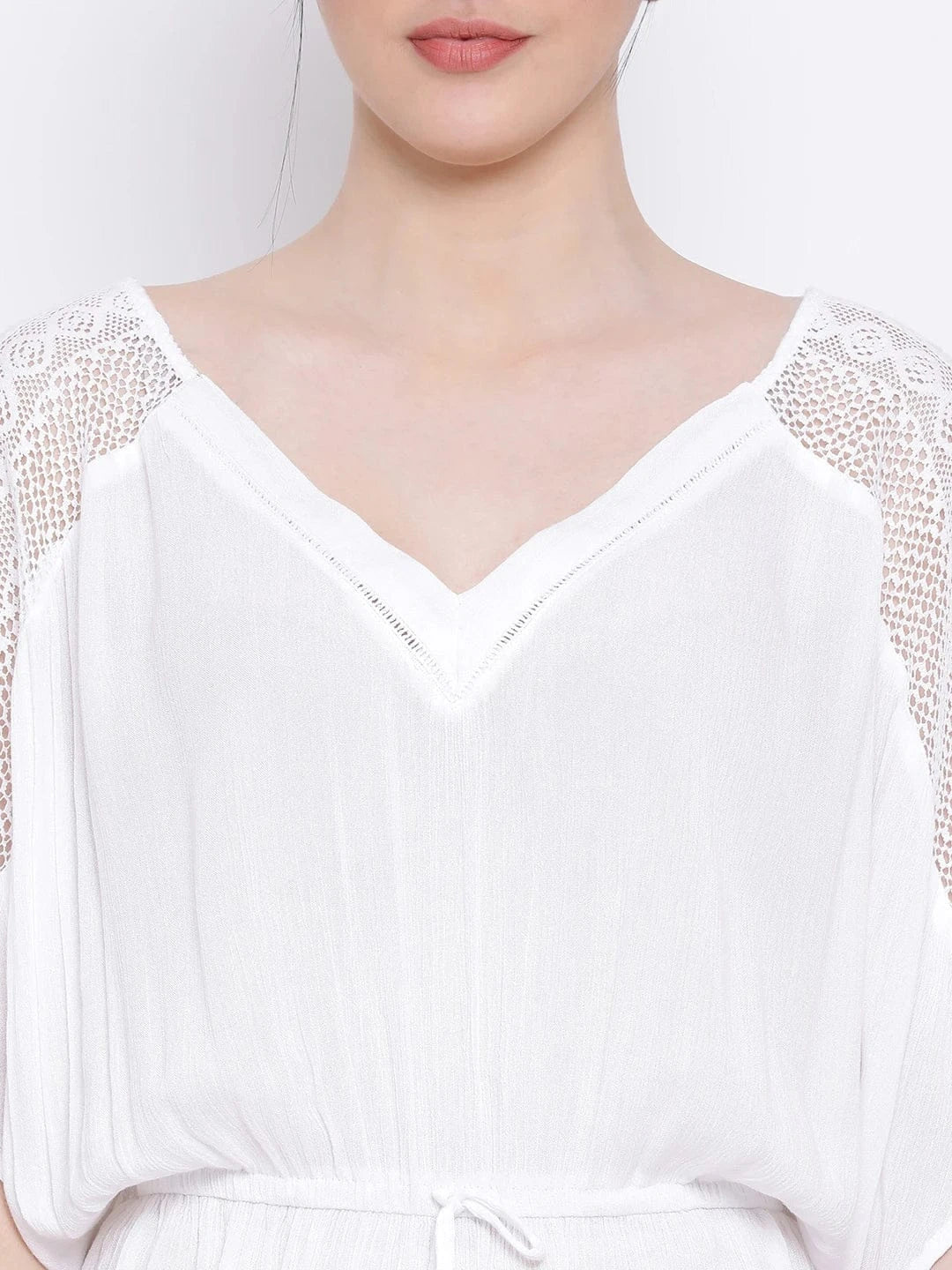 A woman wearing a white dress with lace sleeves and a v-neck, posing against a white background.