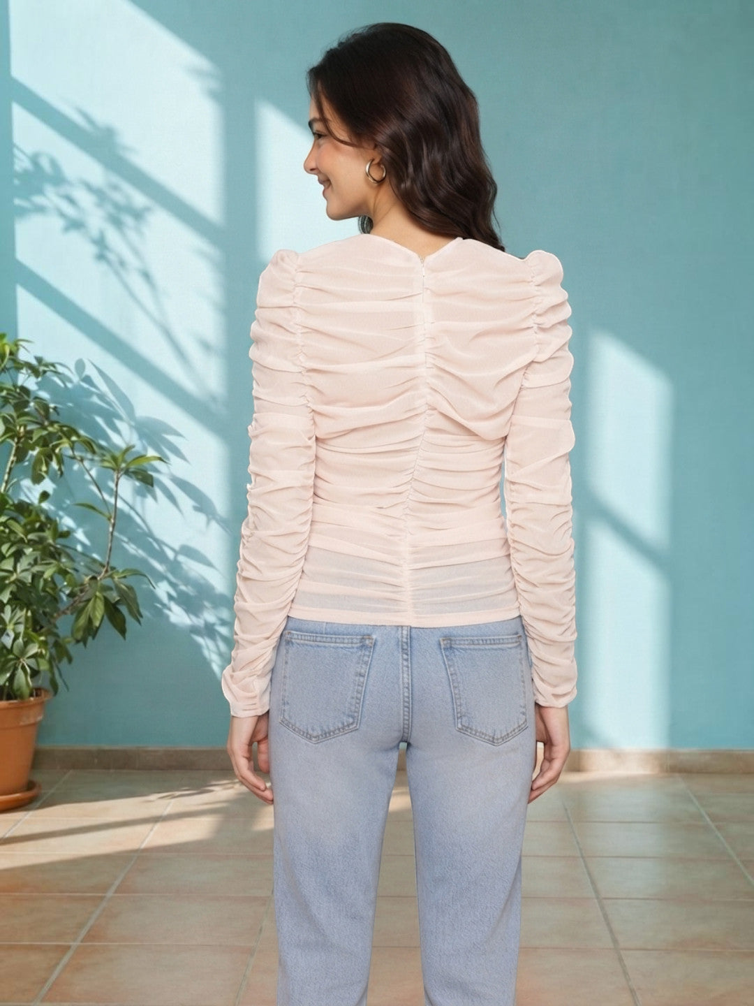 Woman in blush ruched long sleeve top with light wash jeans, back view, stylish plus size fashion