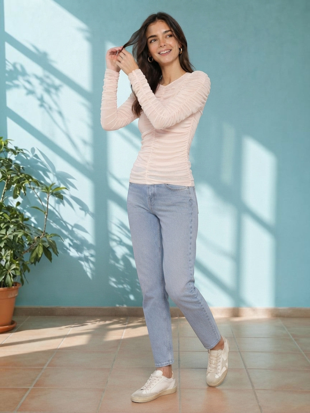 Woman in blush ruched long sleeve top with light wash jeans and white sneakers, stylish casual outfit