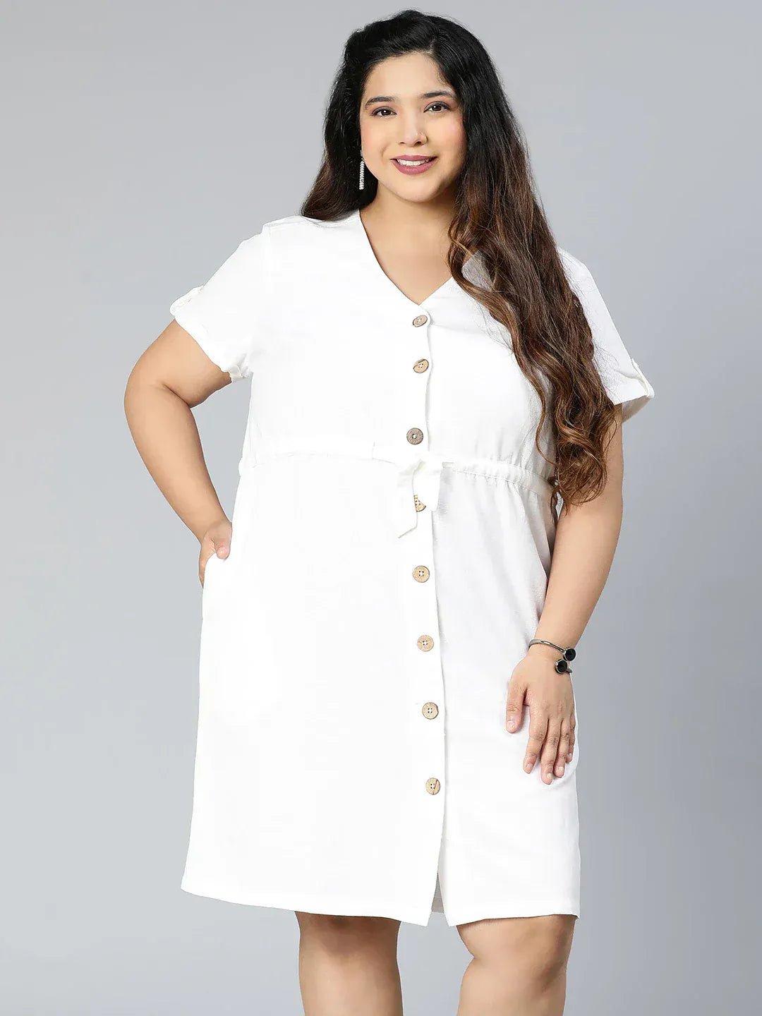 A woman wearing a white dress with buttons and holding a purse is standing against a white background.