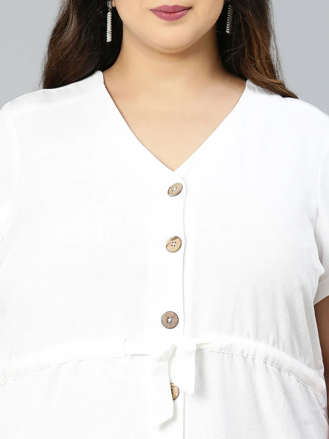 A woman wearing a white dress with buttons and holding a purse is standing against a white background.