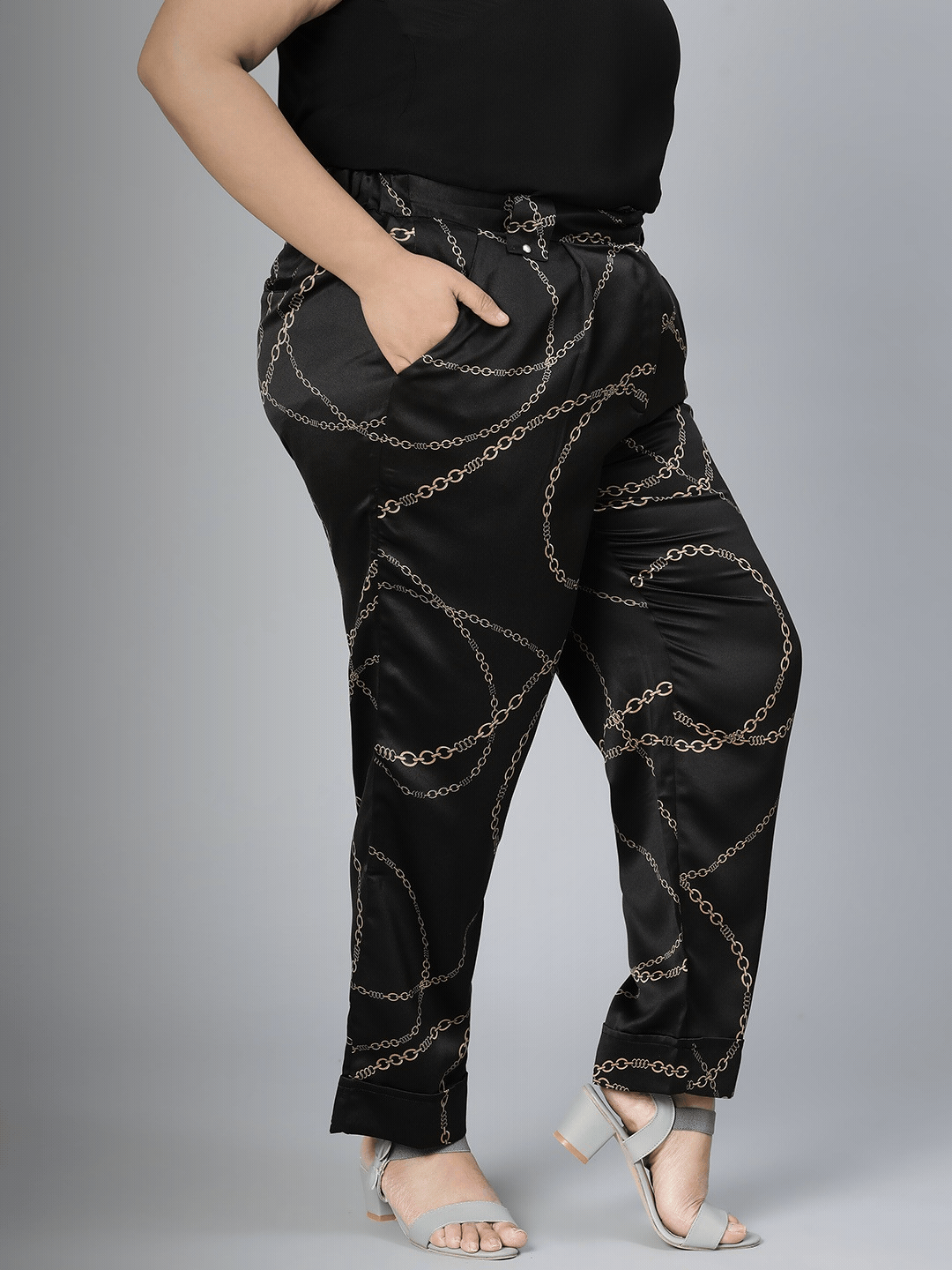 A person wearing black pants with a gold chain print pattern.