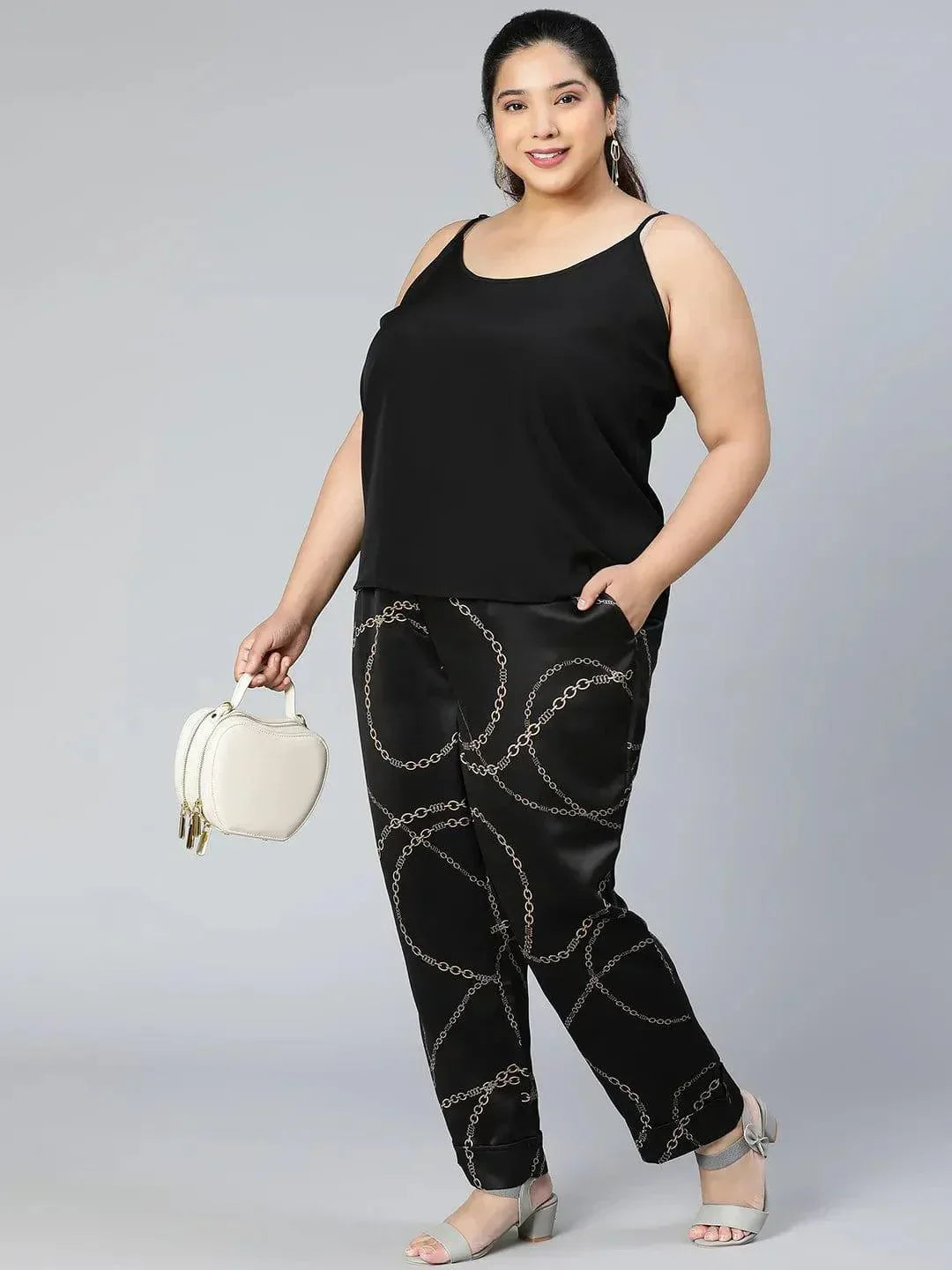 A person wearing black pants with a gold chain print pattern.