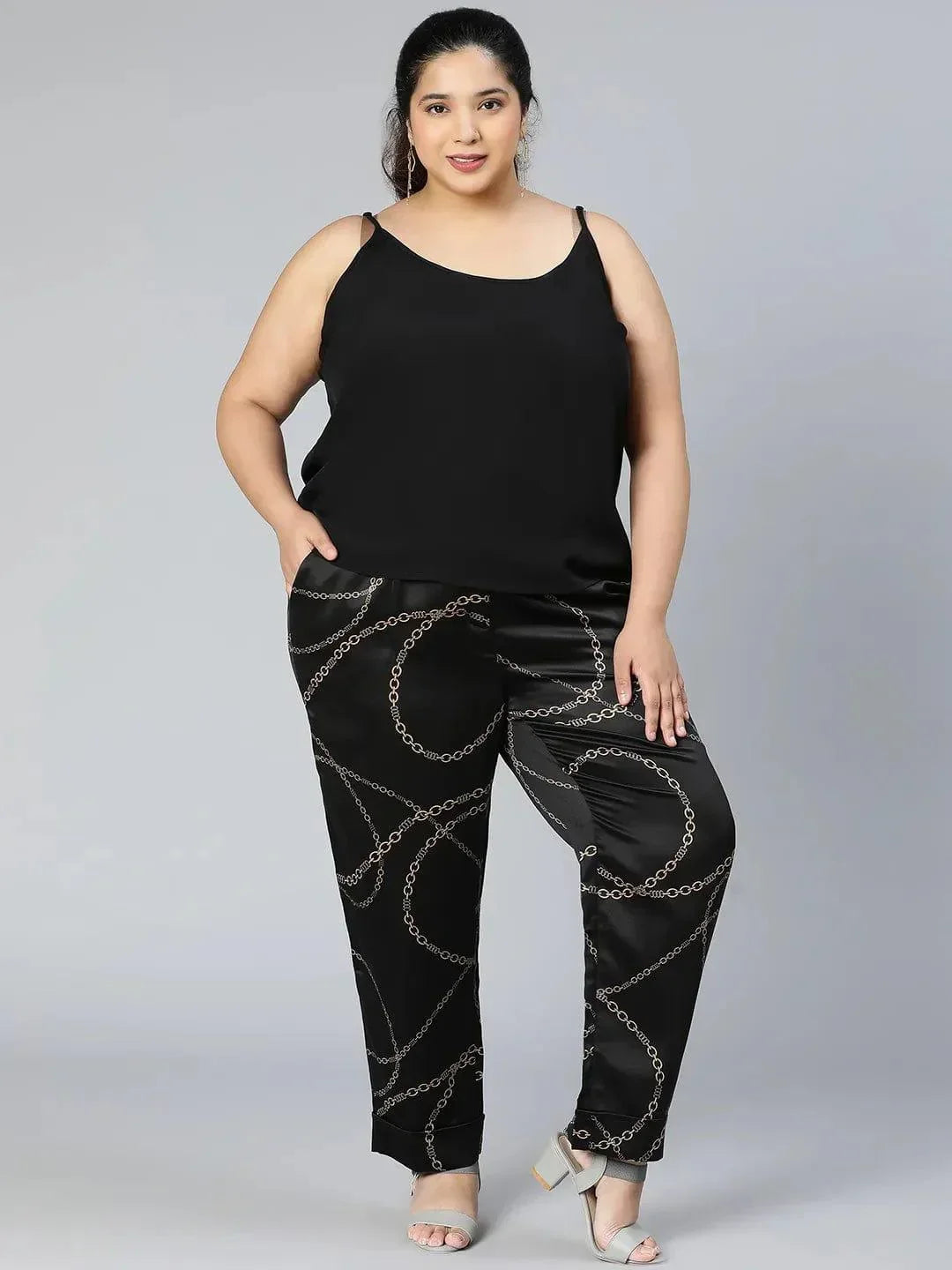 A person wearing black pants with a gold chain print pattern.