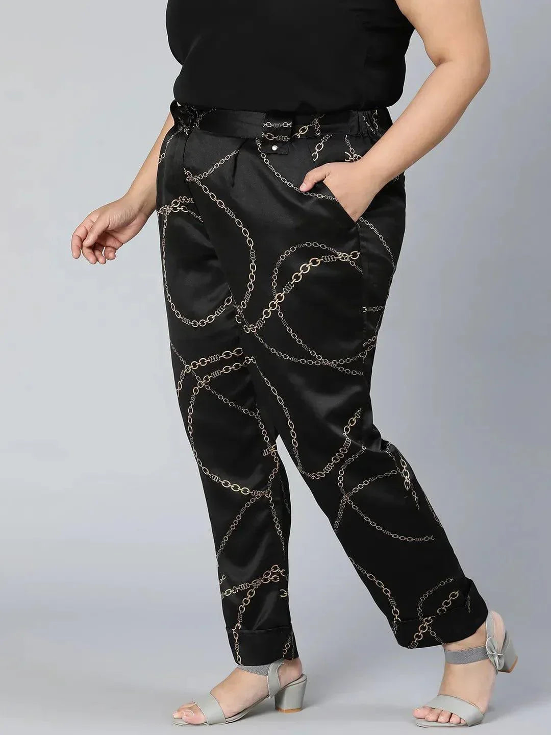 A person wearing black pants with a gold chain print pattern.