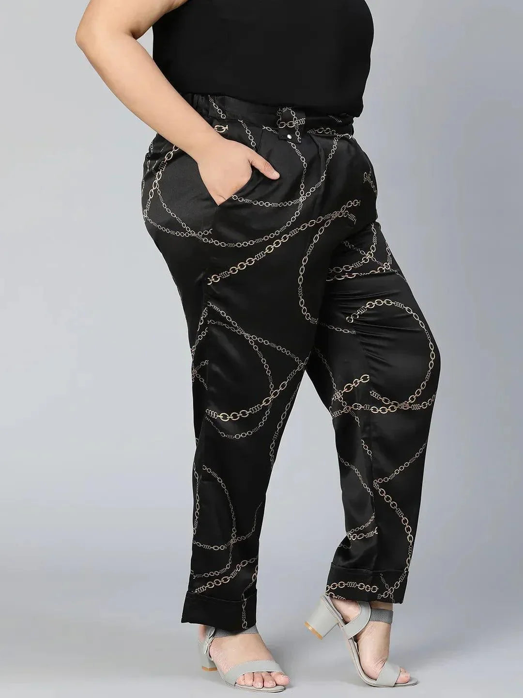 A person wearing black pants with a gold chain print pattern.