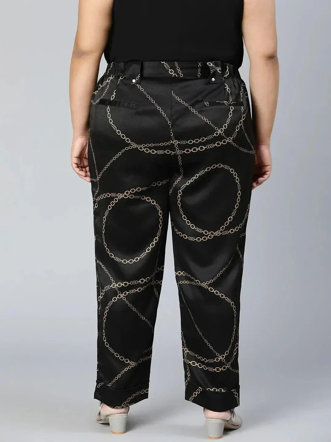 A person wearing black pants with a gold chain print pattern.