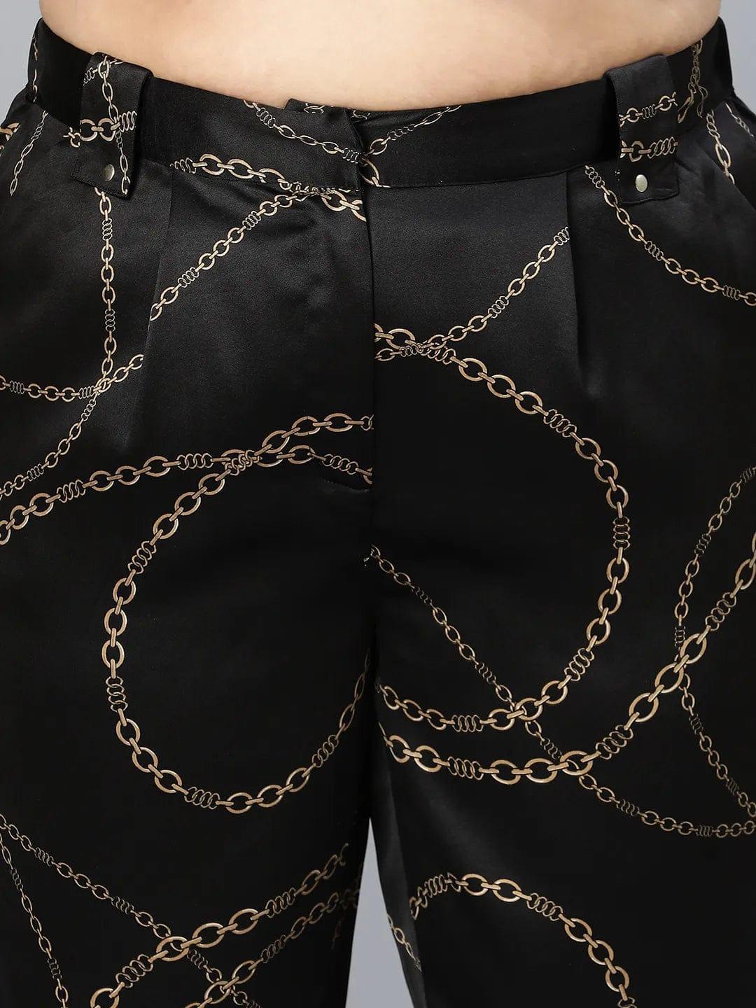 A person wearing black pants with a gold chain print pattern.