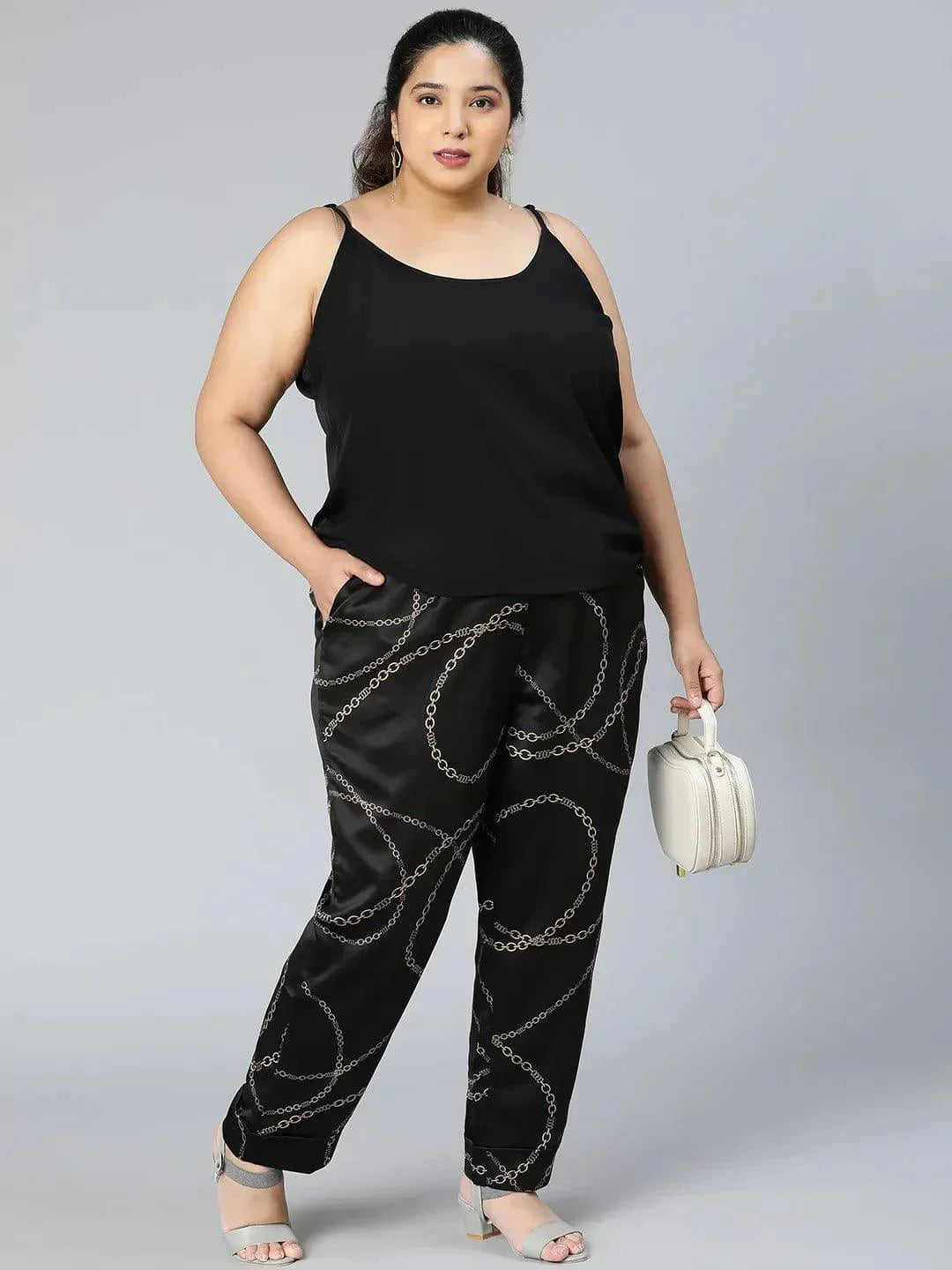 A person wearing black pants with a gold chain print pattern.