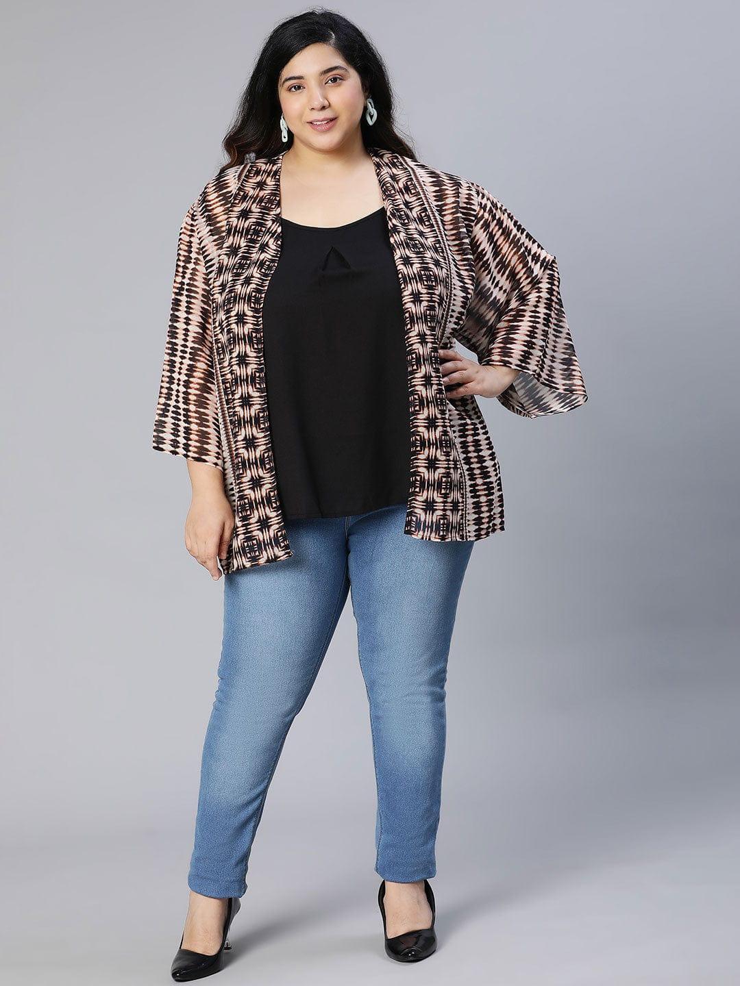 A woman wearing a patterned cardigan, a black top, and blue jeans, posing for a portrait against a white background.