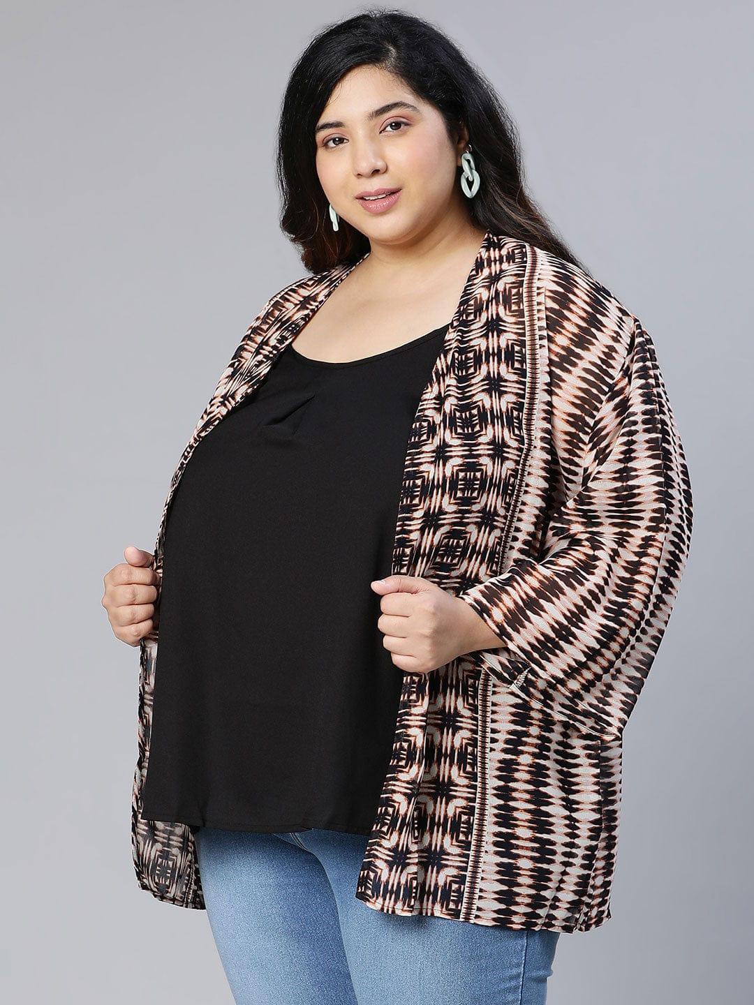 A woman wearing a patterned cardigan, a black top, and blue jeans, posing for a portrait against a white background.