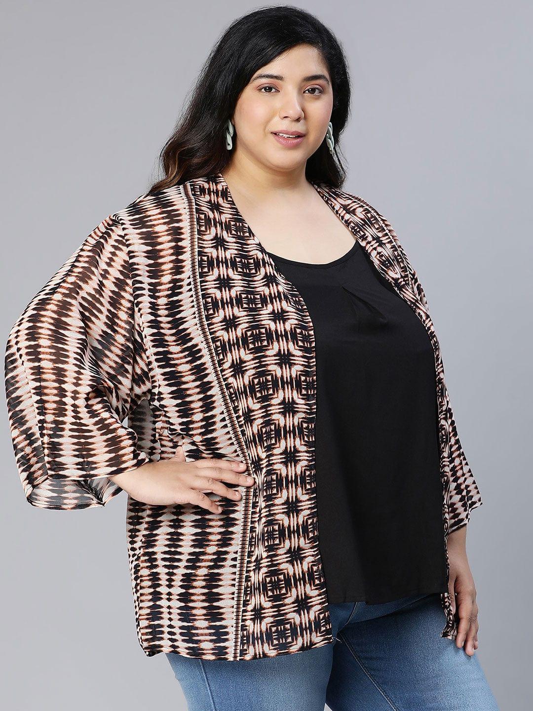 A woman wearing a patterned cardigan, a black top, and blue jeans, posing for a portrait against a white background.