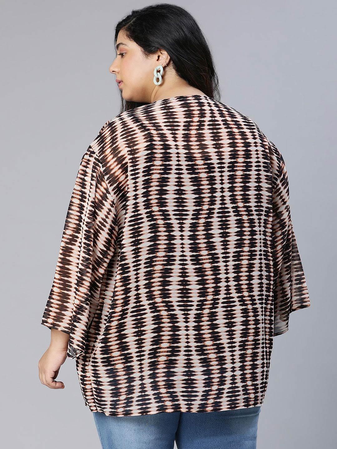 A woman wearing a patterned cardigan, a black top, and blue jeans, posing for a portrait against a white background.