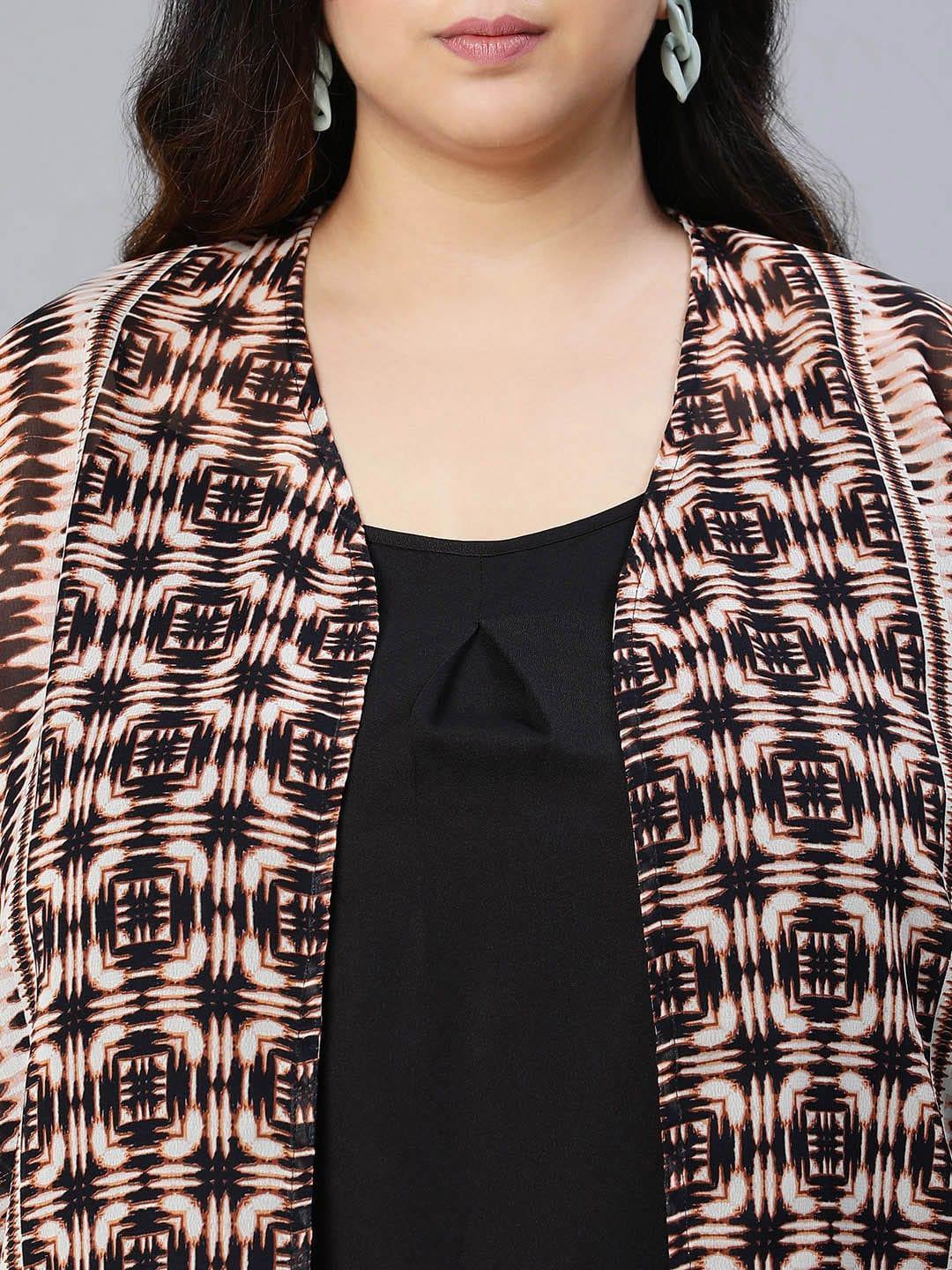 A woman wearing a patterned cardigan, a black top, and blue jeans, posing for a portrait against a white background.