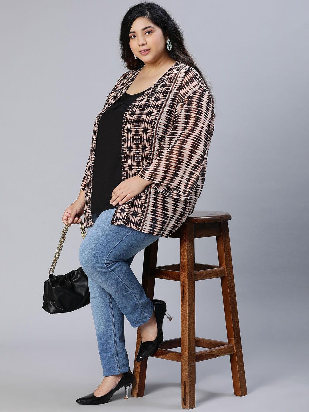 A woman wearing a patterned cardigan, a black top, and blue jeans, posing for a portrait against a white background.