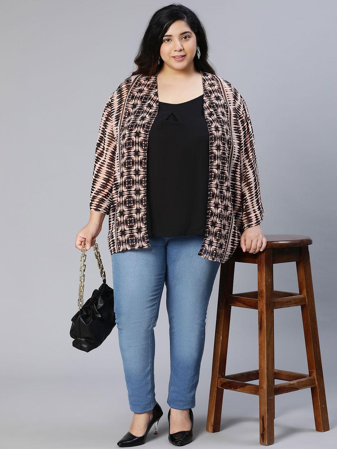 A woman wearing a patterned cardigan, a black top, and blue jeans, posing for a portrait against a white background.