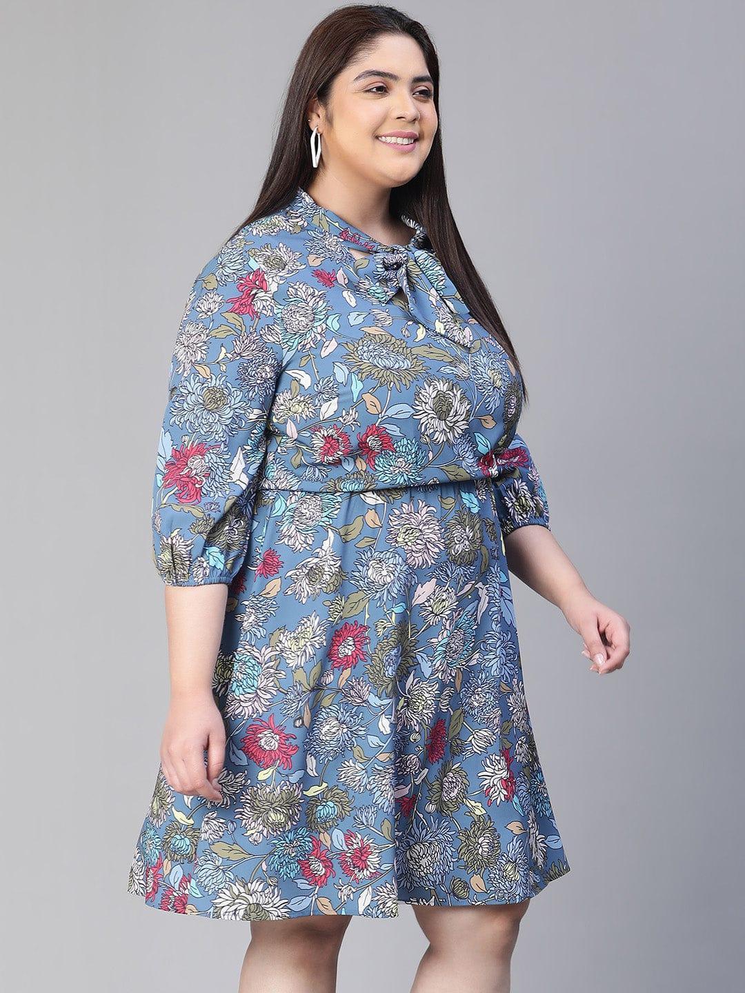 A woman wearing a blue floral print dress with a bow detail, smiling at the camera.