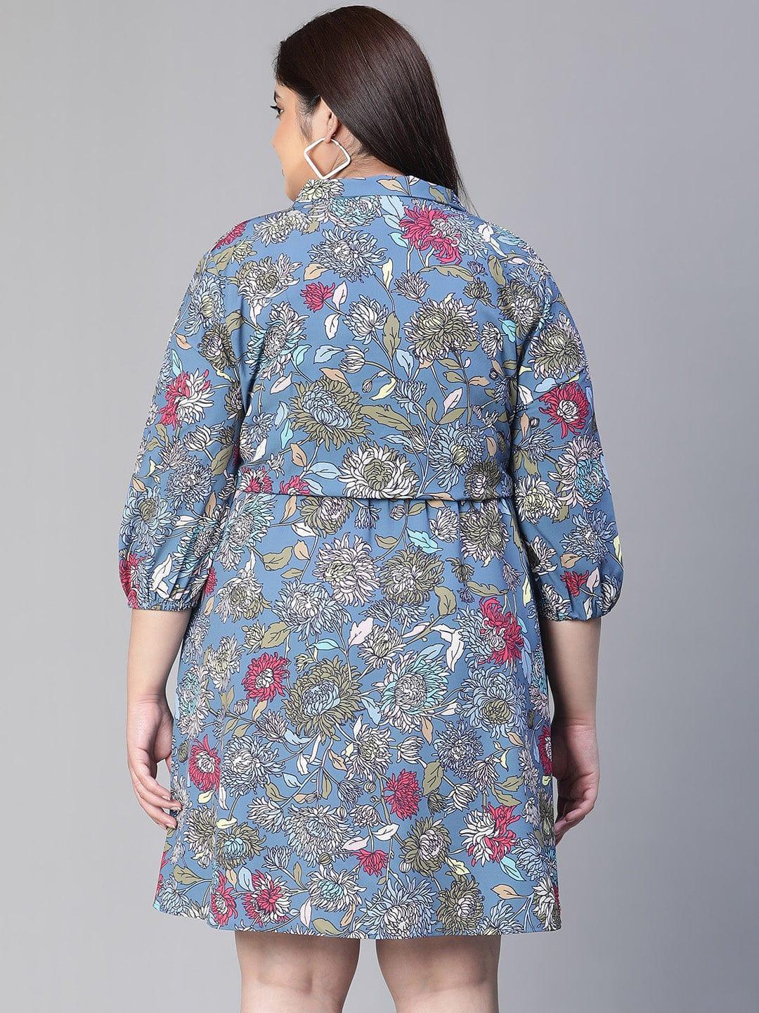 A woman wearing a blue floral print dress with a bow detail, smiling at the camera.