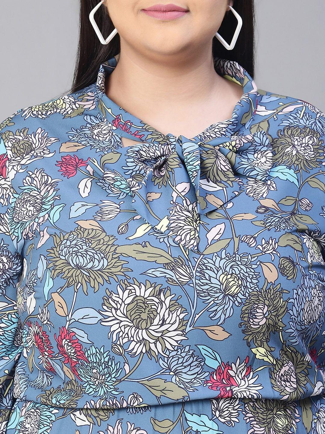 A woman wearing a blue floral print dress with a bow detail, smiling at the camera.
