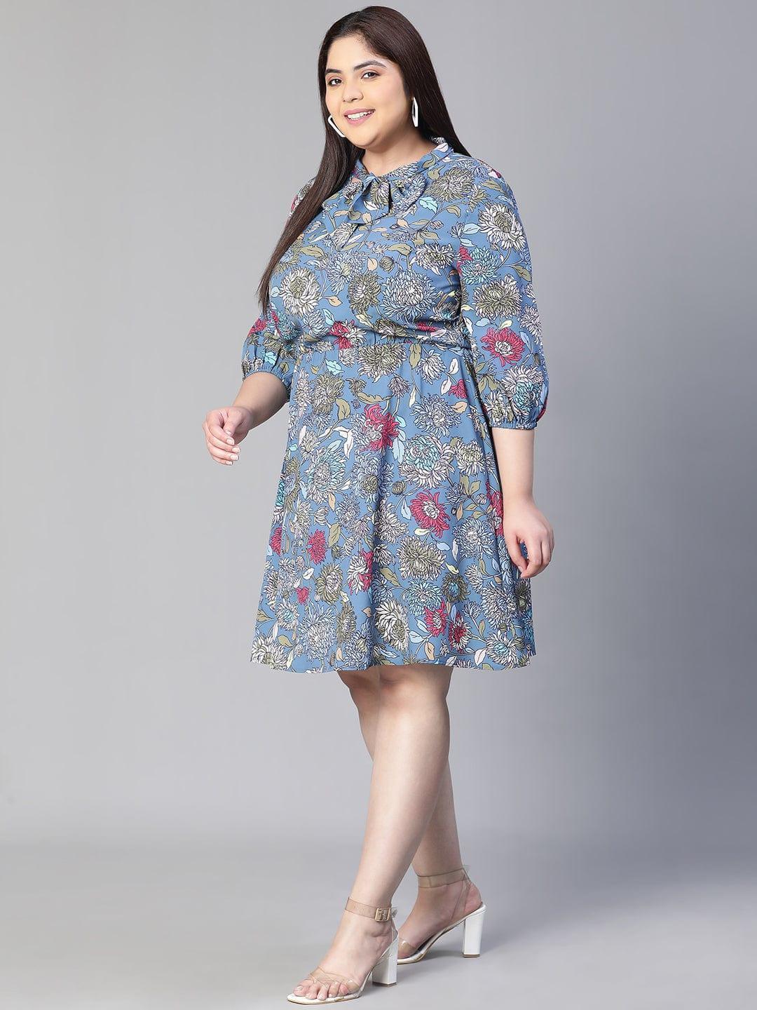 A woman wearing a blue floral print dress with a bow detail, smiling at the camera.