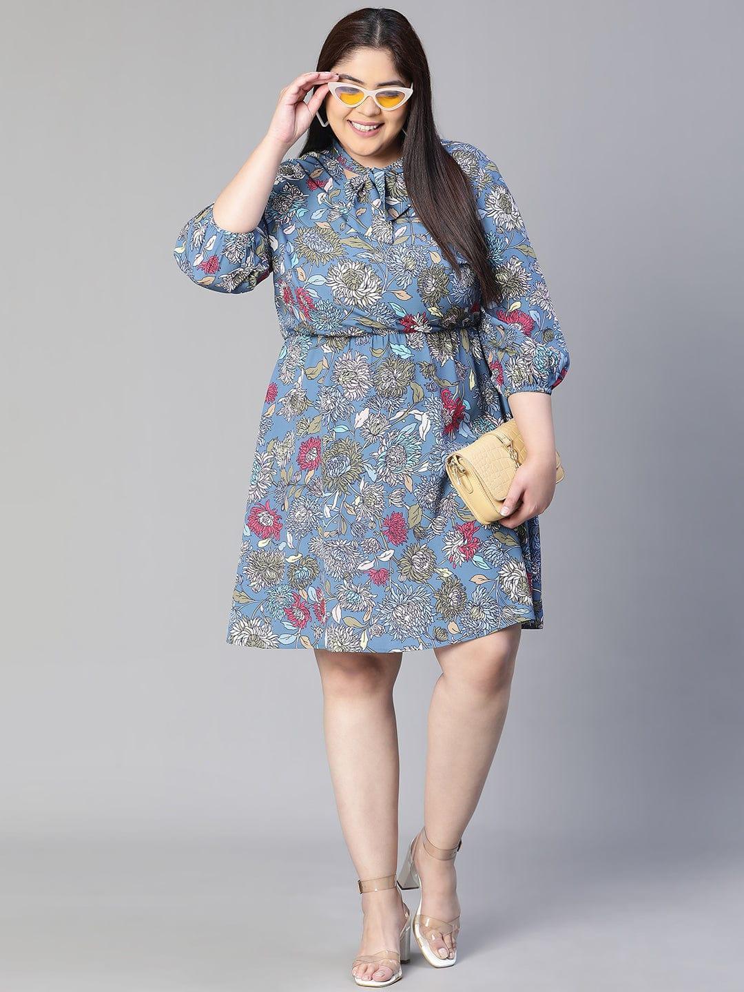 A woman wearing a blue floral print dress with a bow detail, smiling at the camera.
