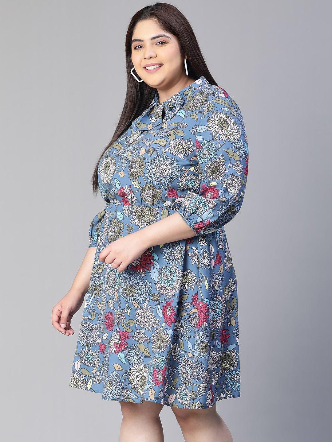 A woman wearing a blue floral print dress with a bow detail, smiling at the camera.