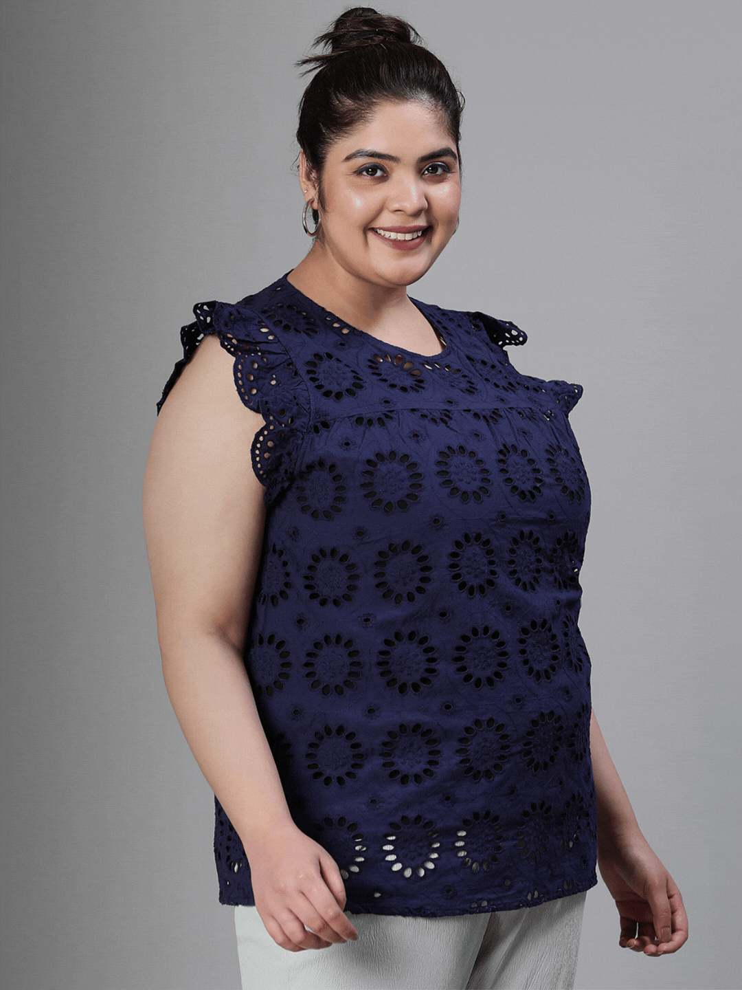 A woman wearing a navy blue top with a floral pattern and a bun hairstyle, smiling at the camera.