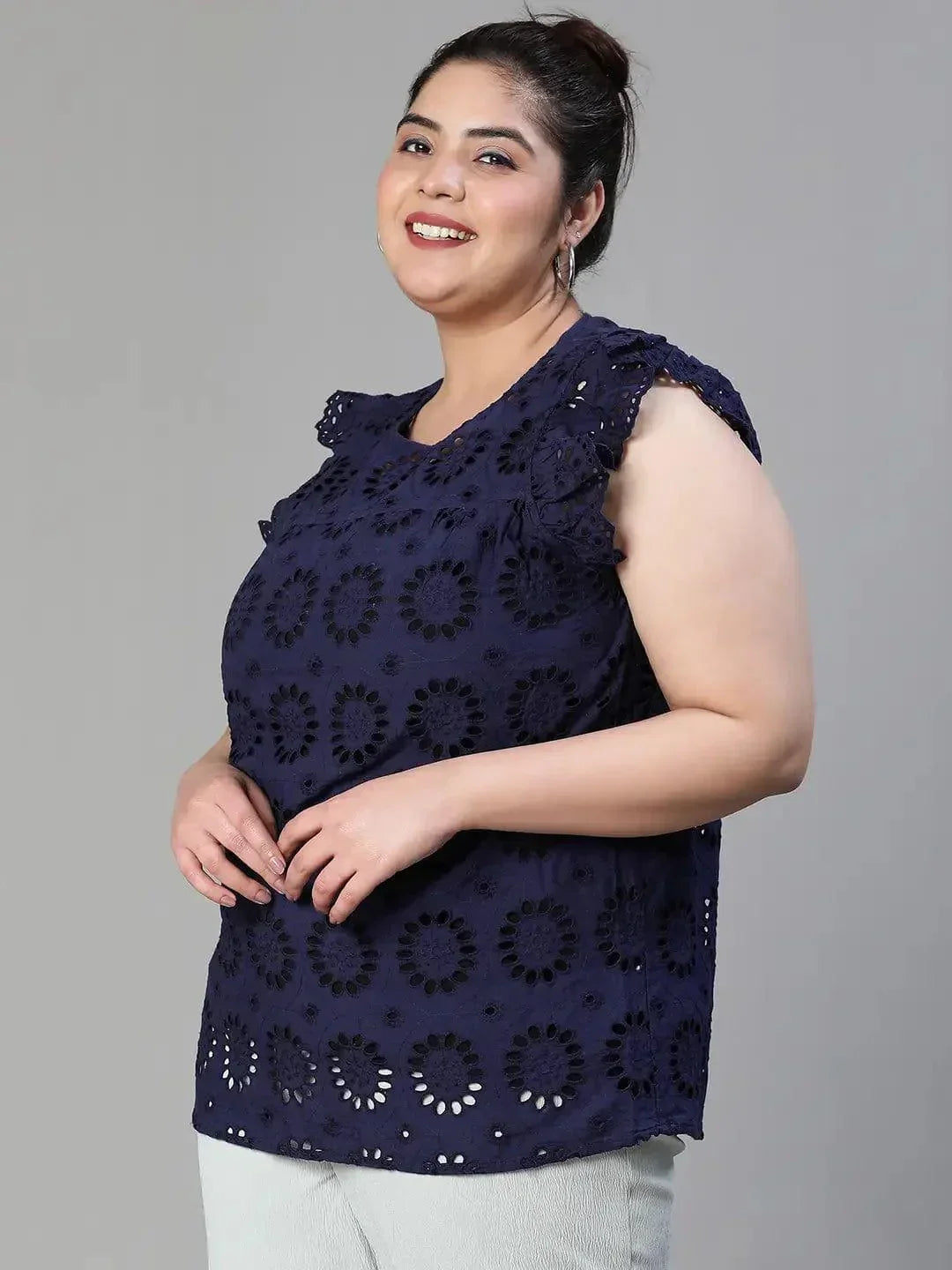 A woman wearing a navy blue top with a floral pattern and a bun hairstyle, smiling at the camera.